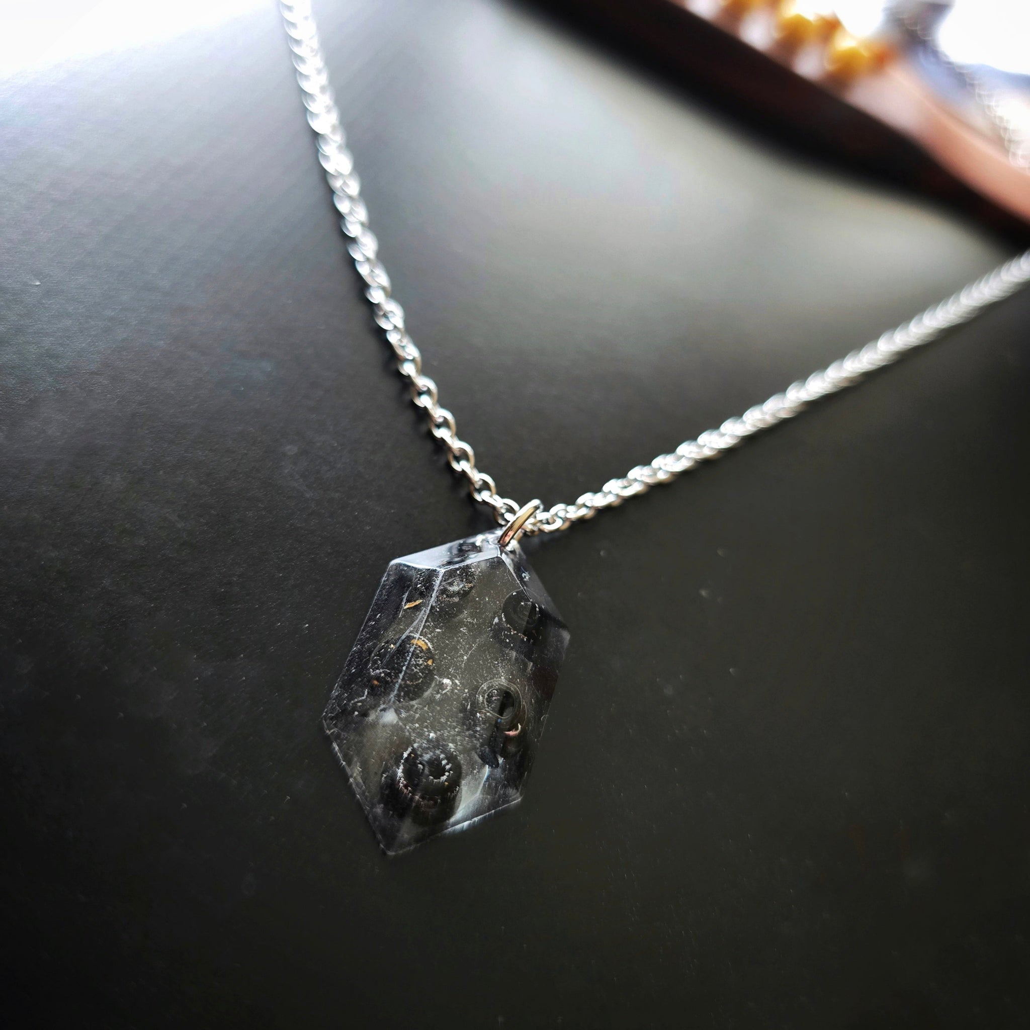 Close-up of Necklace with a resin hexagonal pendant with black guitar string ballends on a dark guitar