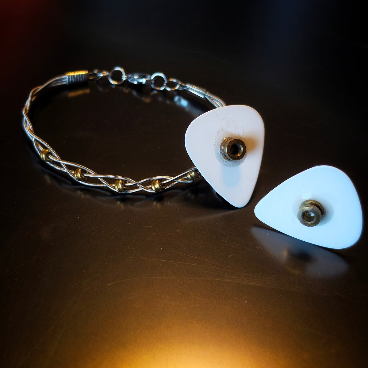 Closeup of Guitar Pick Earrings and Braided Guitar String and Gold Coloured Ballend Clasp Style Bracelet Jewelry Set on Dark Background