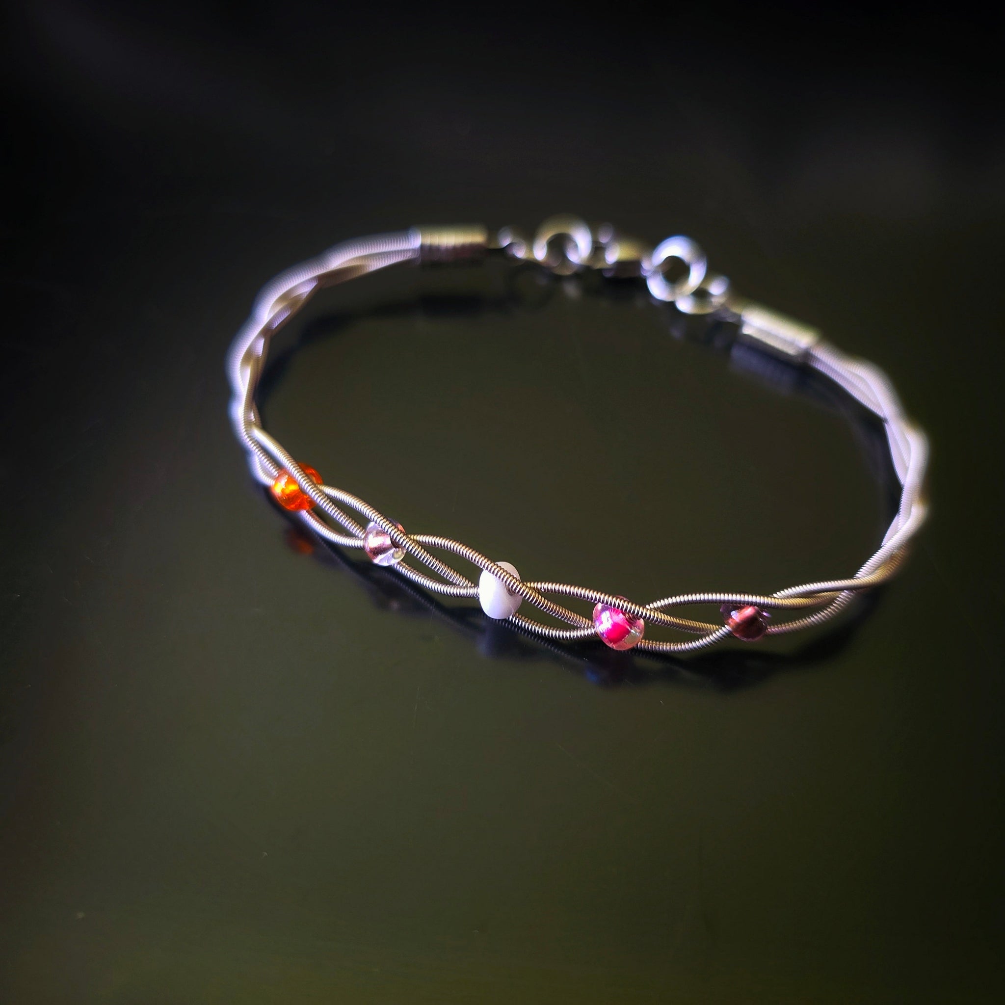Guitar string bracelet with 5 beads representing the colours of the lesbian pride flag on dark background