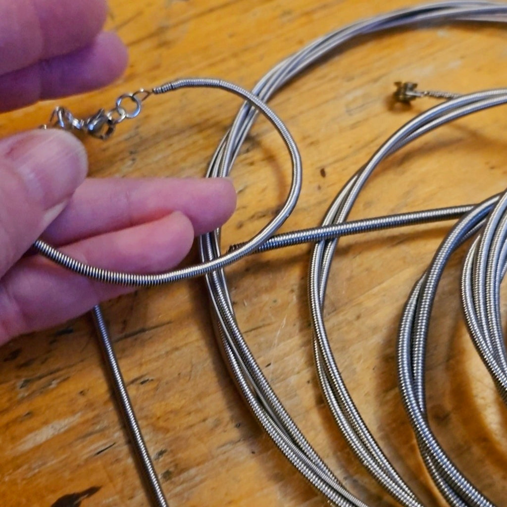 Hand holding a electric bass string bracelet next to a pile of bass strings 