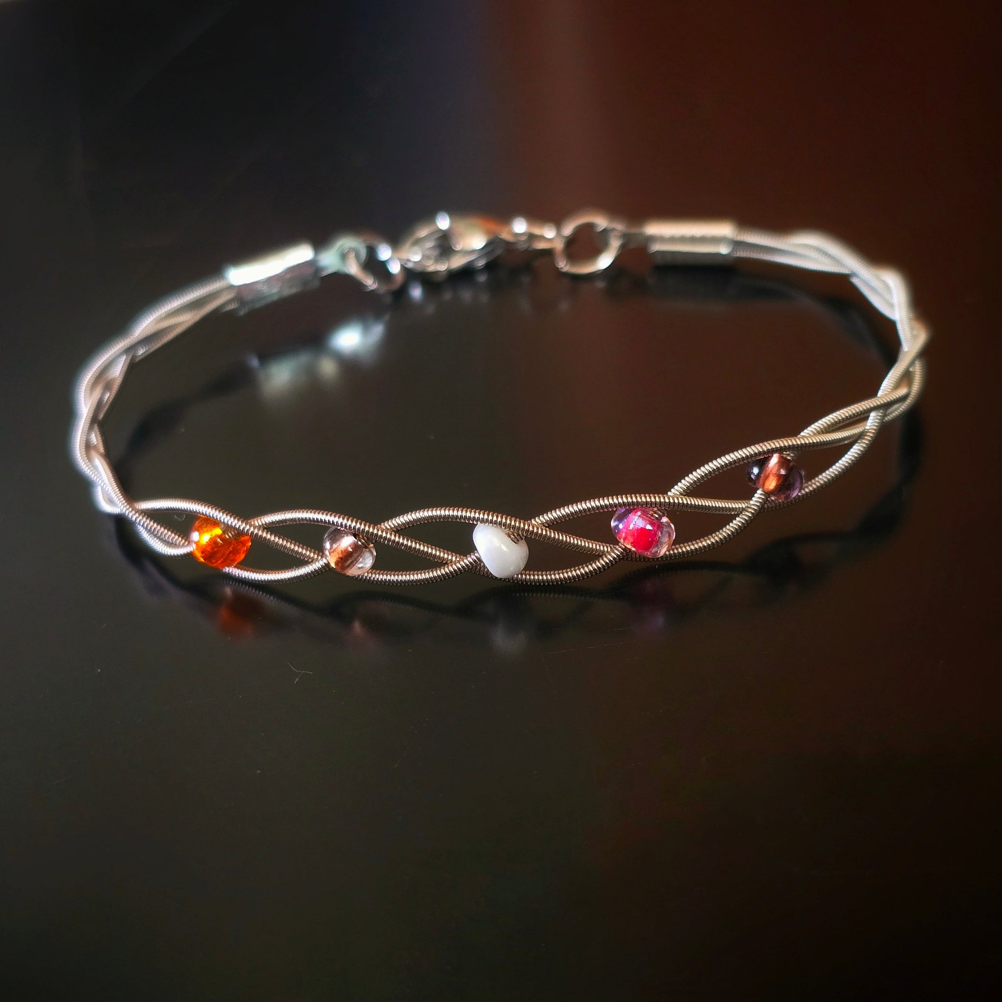 Front view of guitar string bracelet with 5 beads representing the colours of the lesbian pride flag 