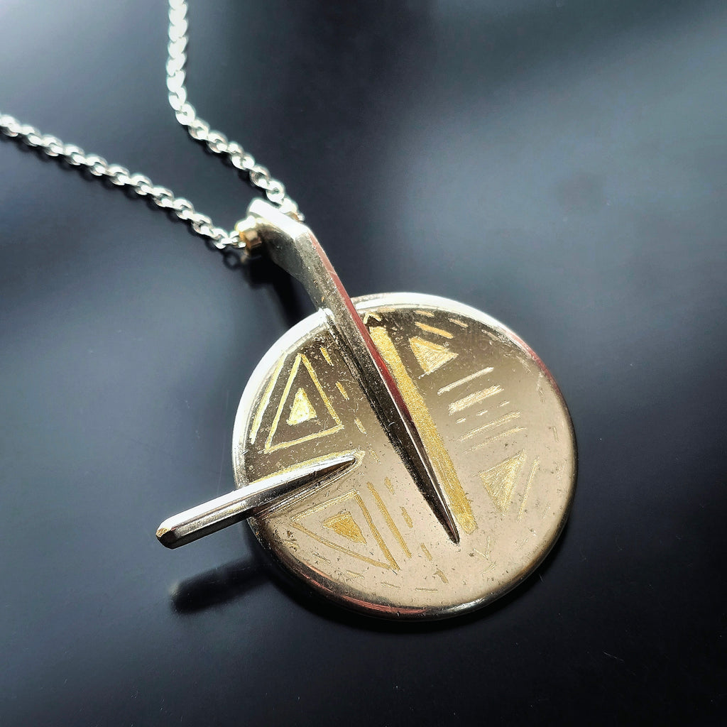 Gold and silver Upcycled saxophone key pendant on a chain against a dark background