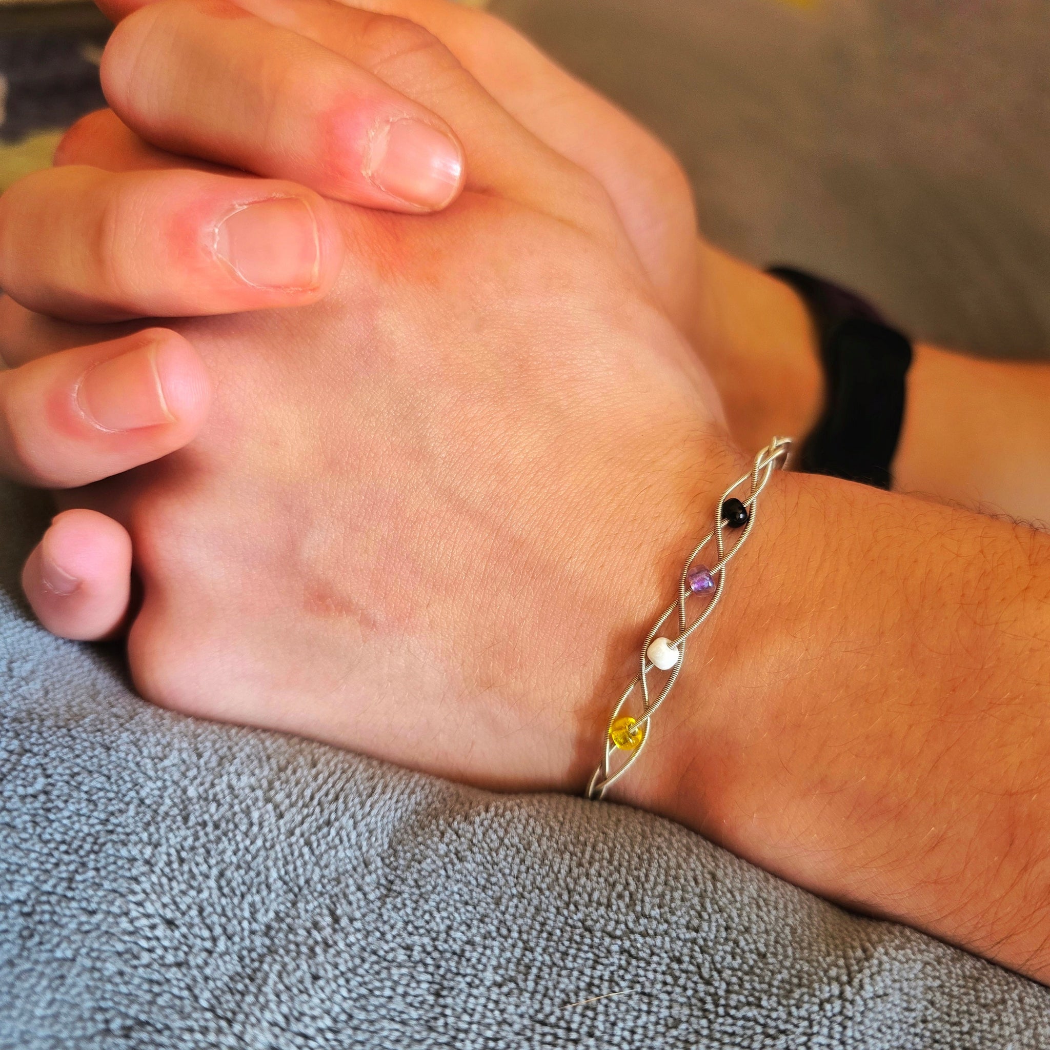 Hand holding Non-Binary Pride Three Guitar String Braided Clasp Bracelet