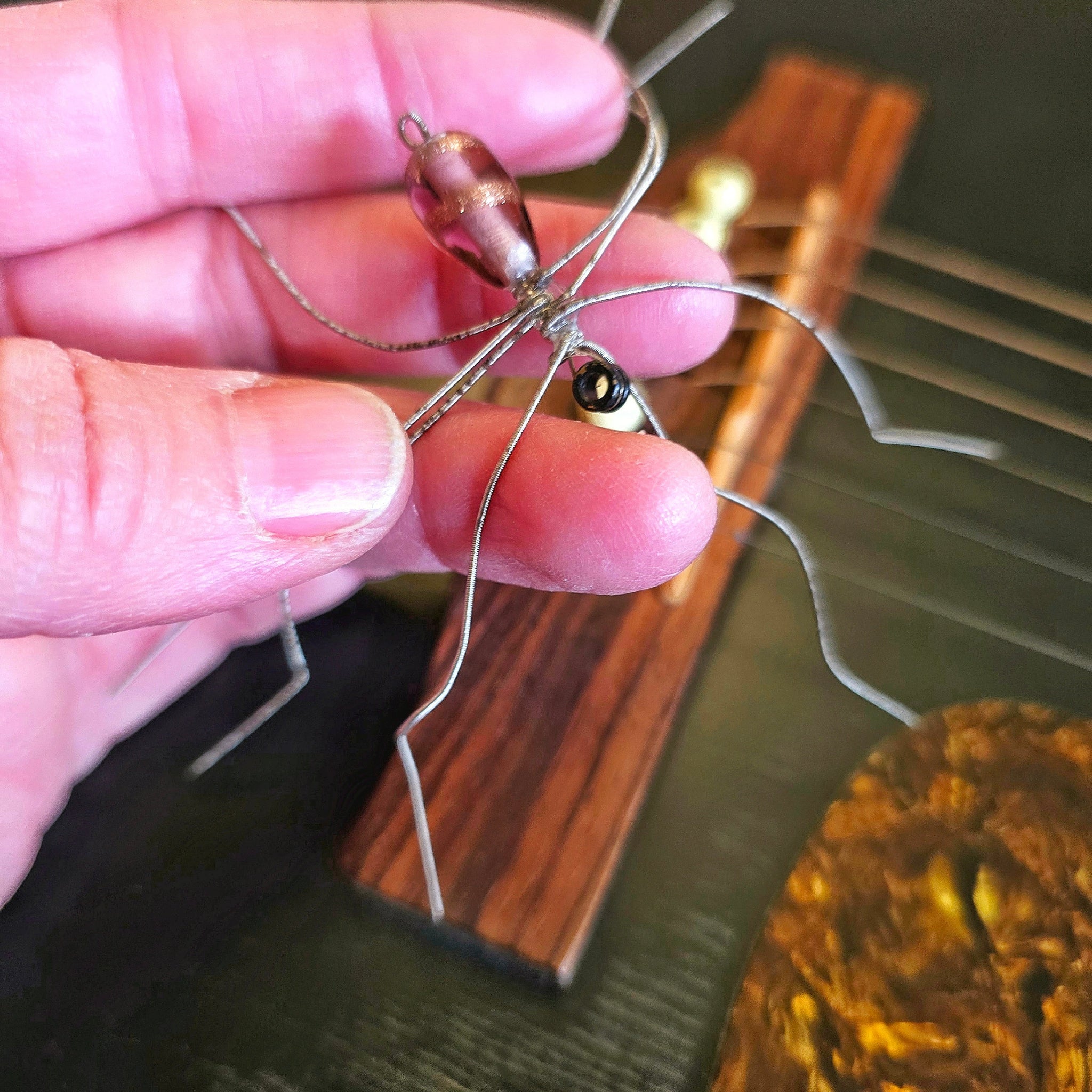 Hand holding a guitar string spider with guitar in background