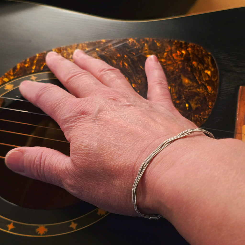 Hand with a guitar string bracelet on an acoustic guitar