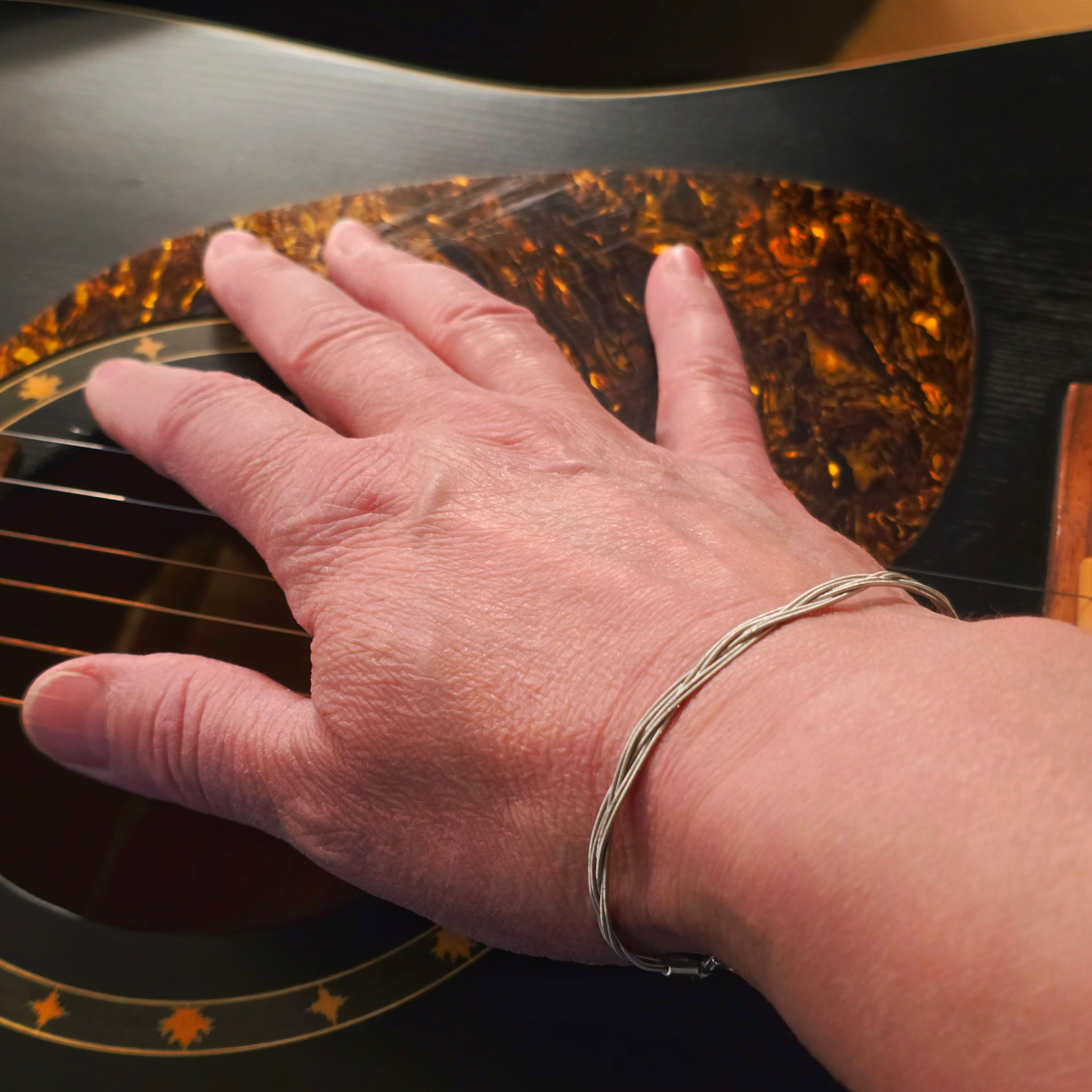 Hand with a guitar string bracelet on an acoustic guitar