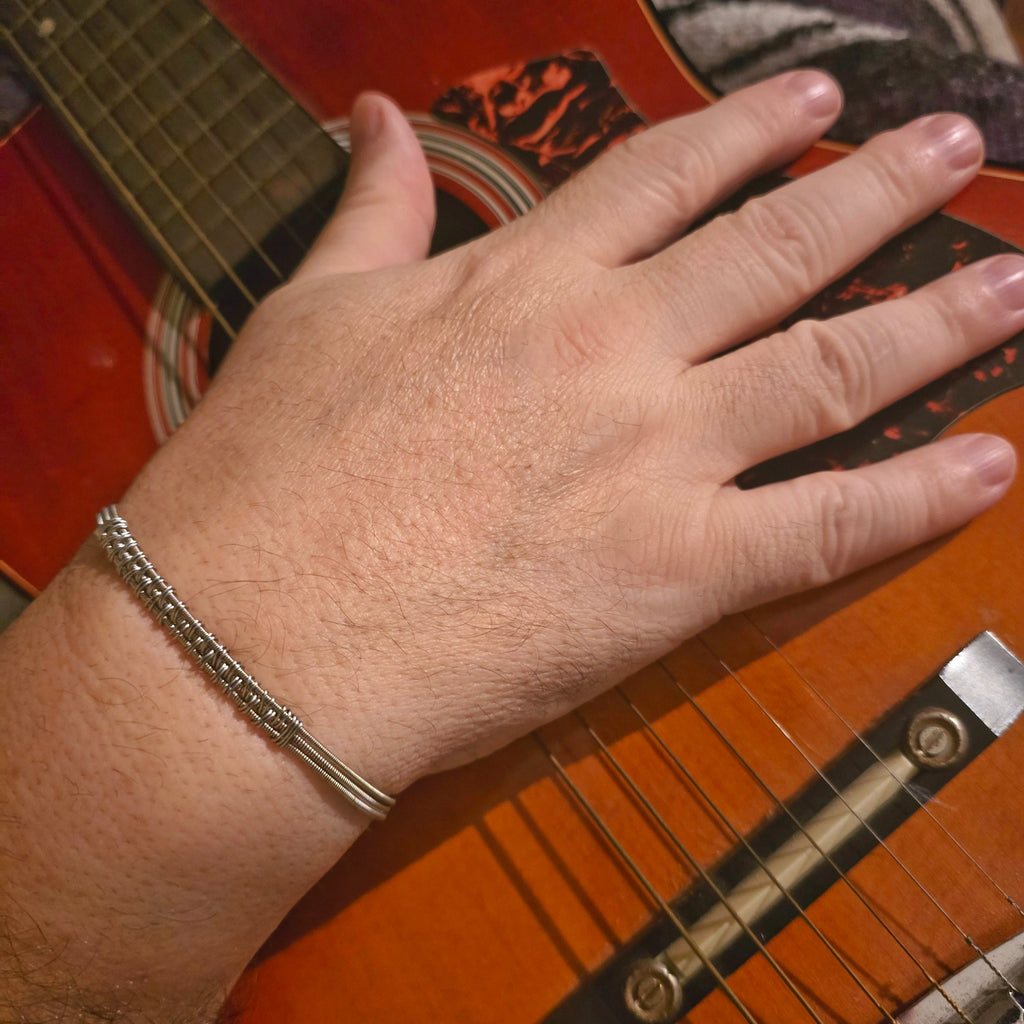 Hand with a guitar string bracelet on an acoustic guitar