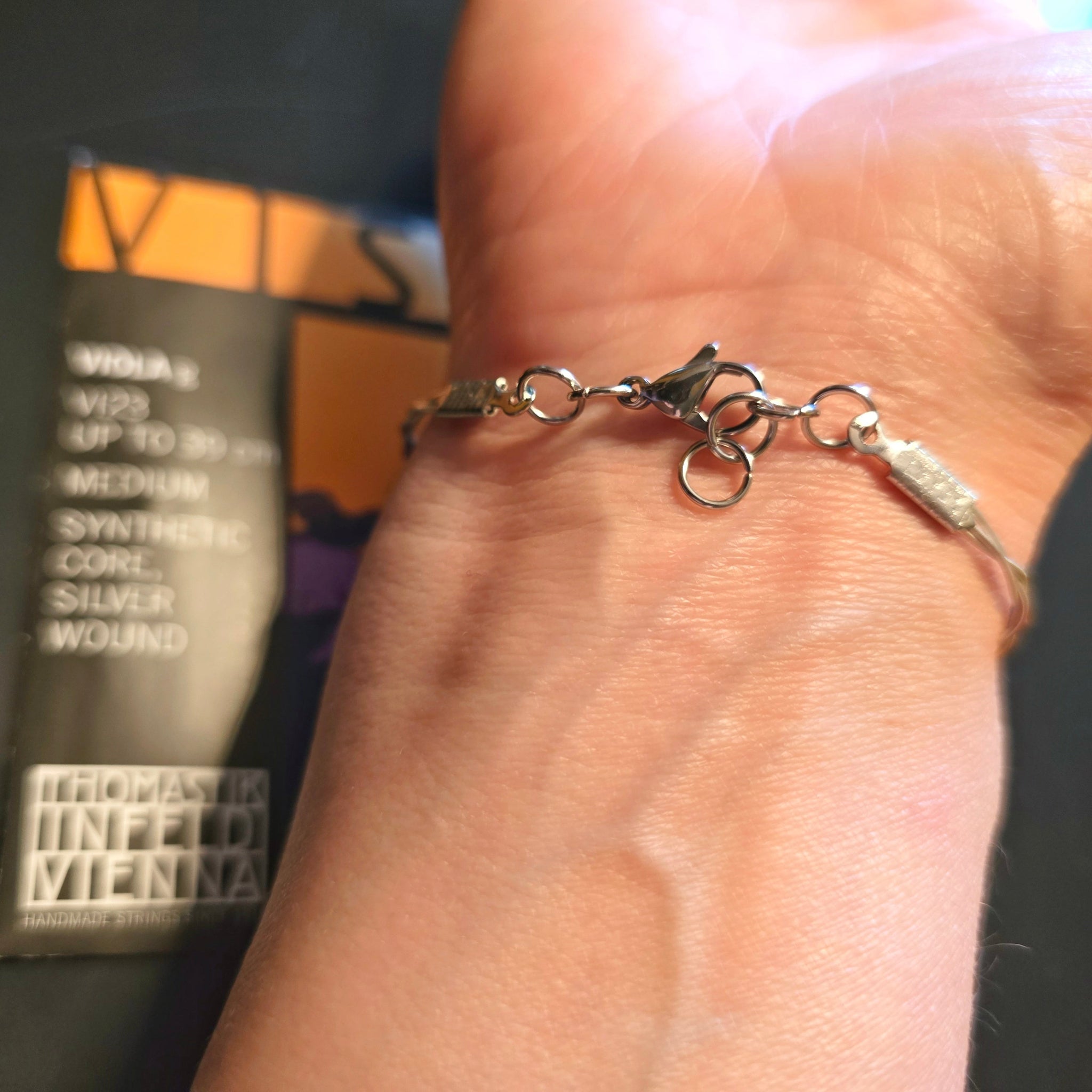 Hand with an Upcycled Viola String Bracelet view of clasp and extra loops (viola string package in background)
