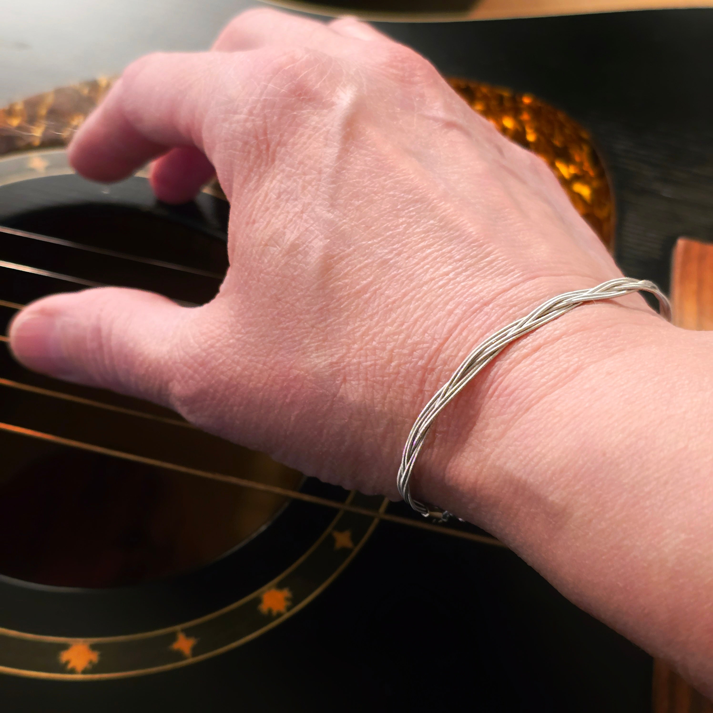 Hand with six string guitar string bracelet plucking strings of black guitar 