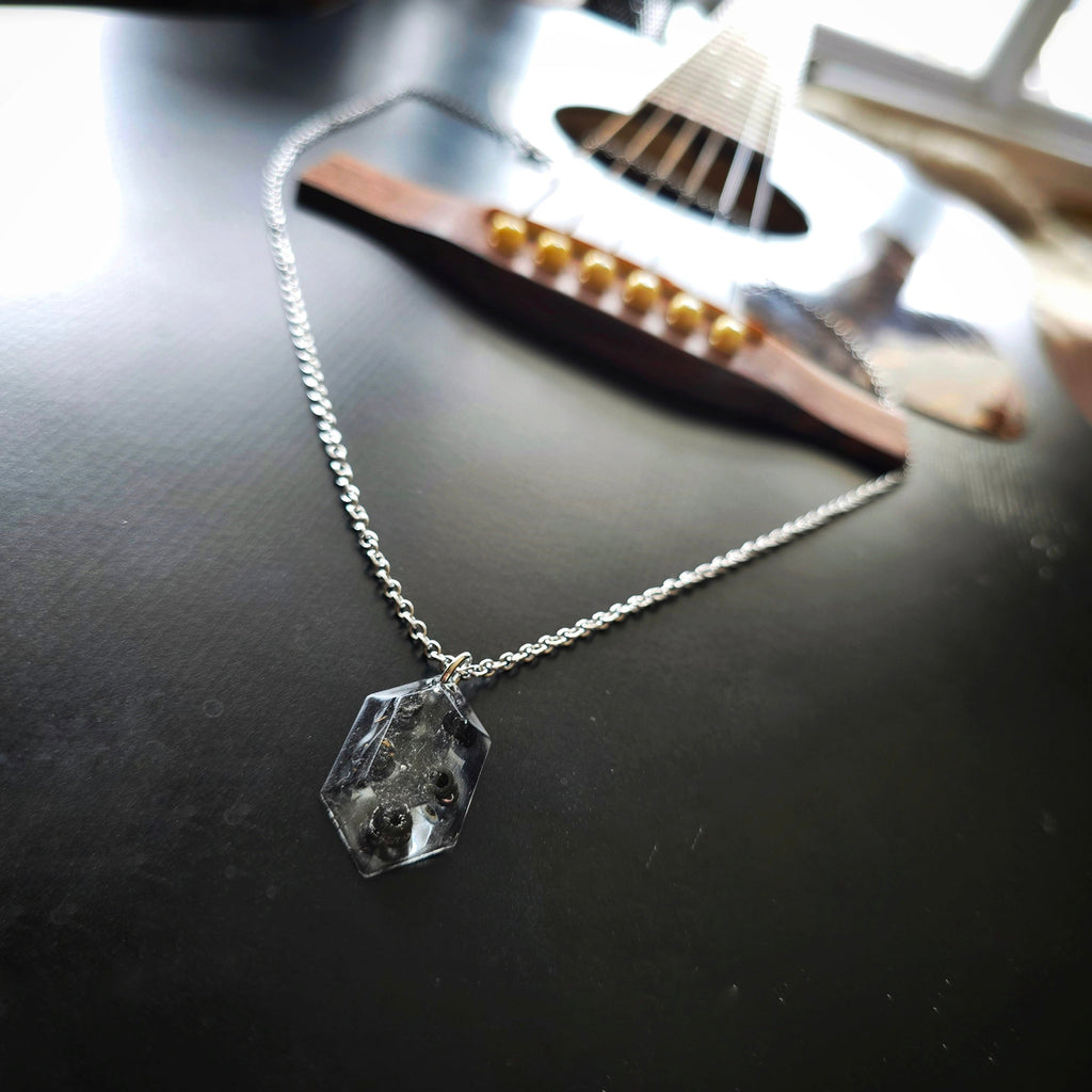 Necklace with a resin hexagonal pendant with black guitar string ballends on a black guitar
