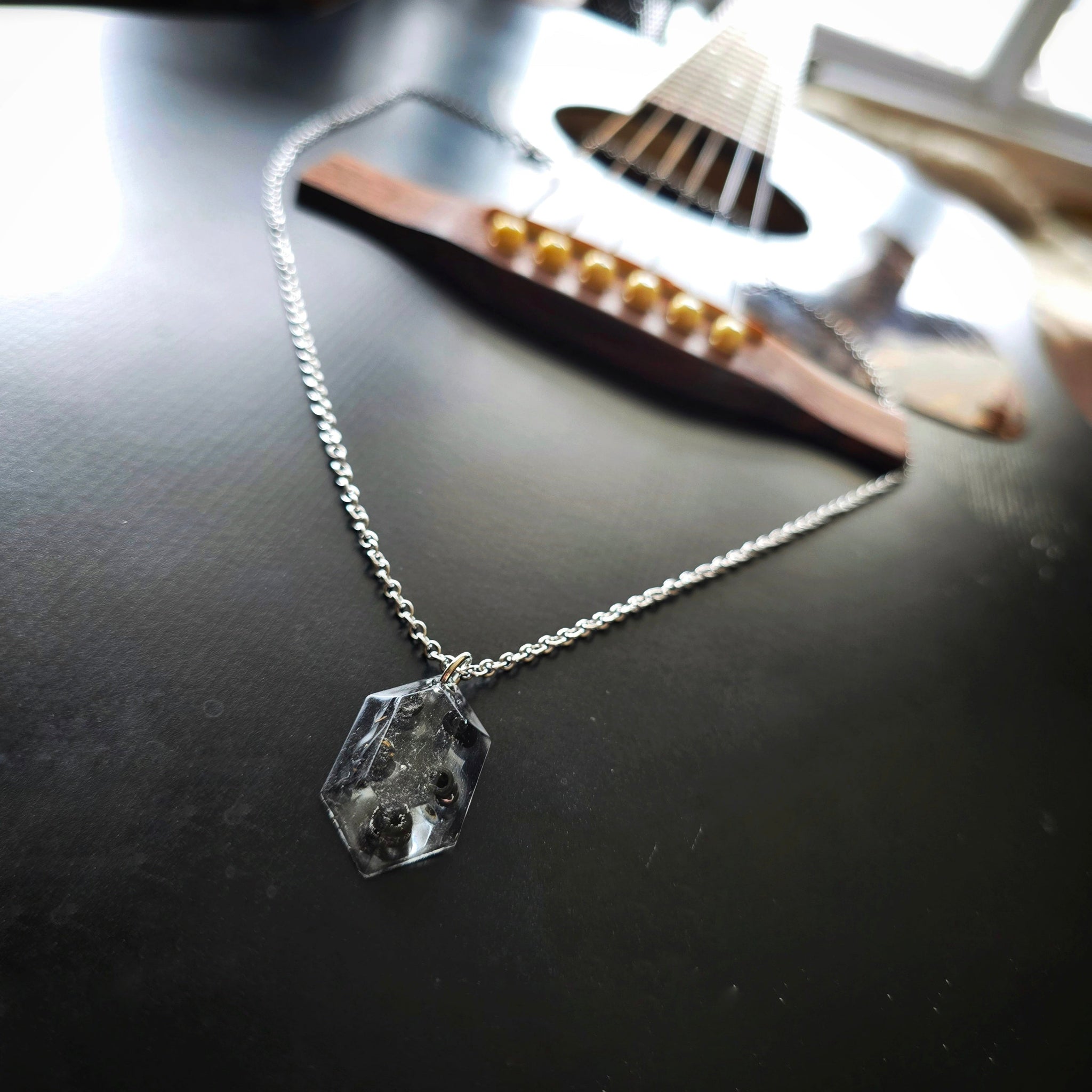 Necklace with a resin hexagonal pendant with black guitar string ballends on a black guitar