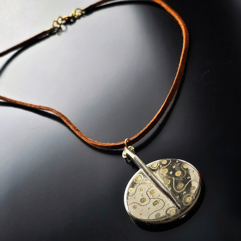 Necklace with a unique upcycled saxophone key pendant on a reflective black surface