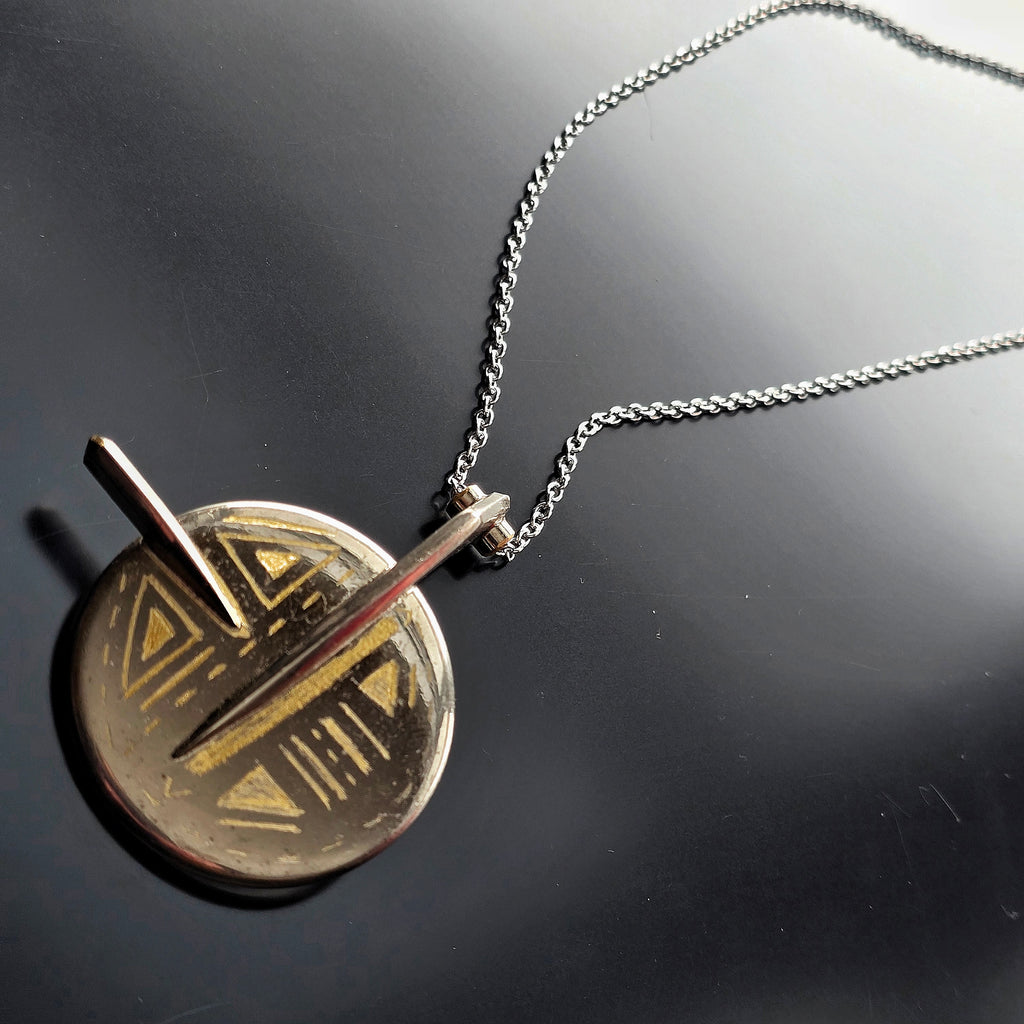 Necklace with an upcycled saxophone key pendant featuring geometric designs on a dark surface
