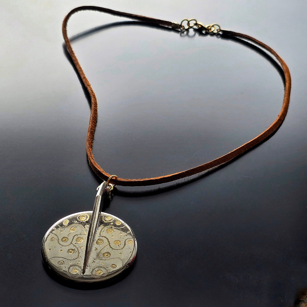 Necklace with an upcycled saxophone key pendant on a dark surface