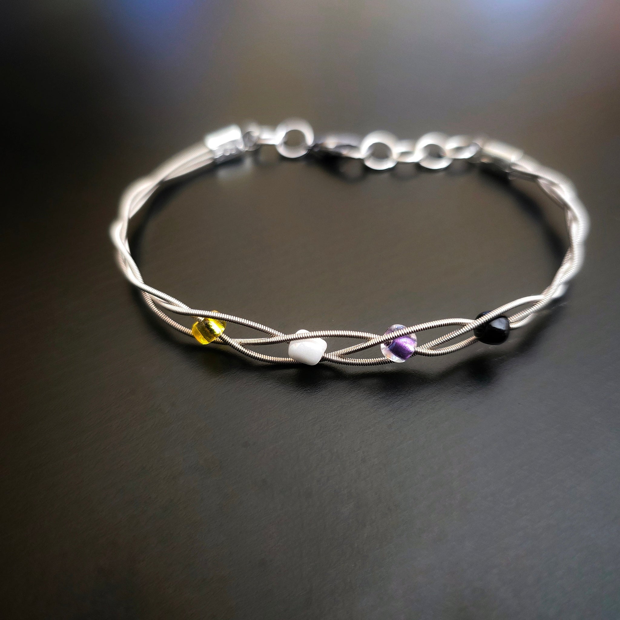 Non-Binary Pride Three Guitar String Braided Clasp Bracelet on Black Background