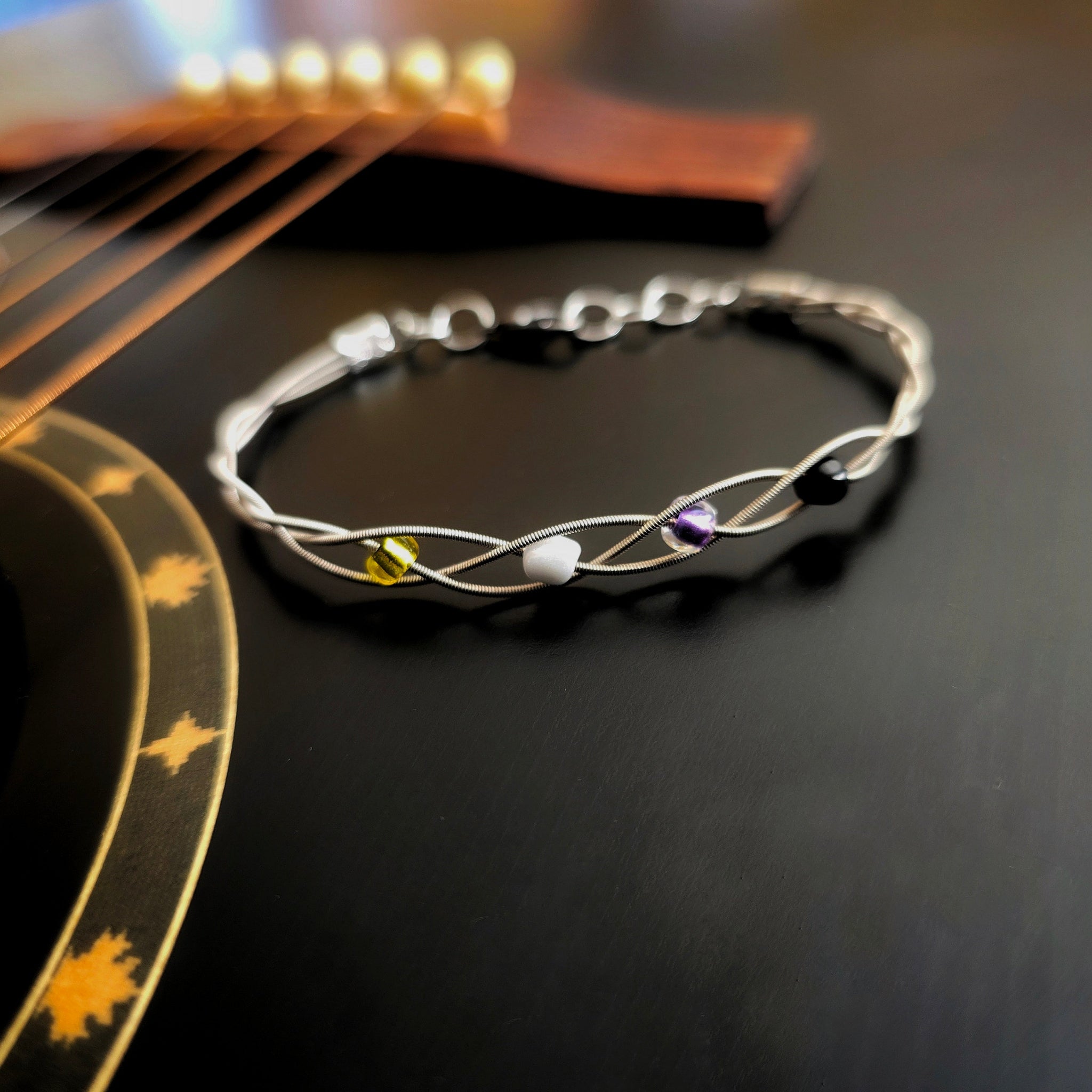 Non-Binary Pride Three Guitar String Braided Clasp Bracelet on Black Guitar