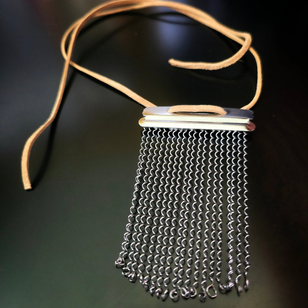 Snare drum string fringe necklaces with light brown suede straps displayed on a black surface 