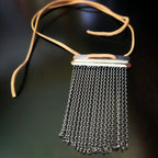 Snare drum string fringe necklaces with light brown suede straps displayed on a black surface 