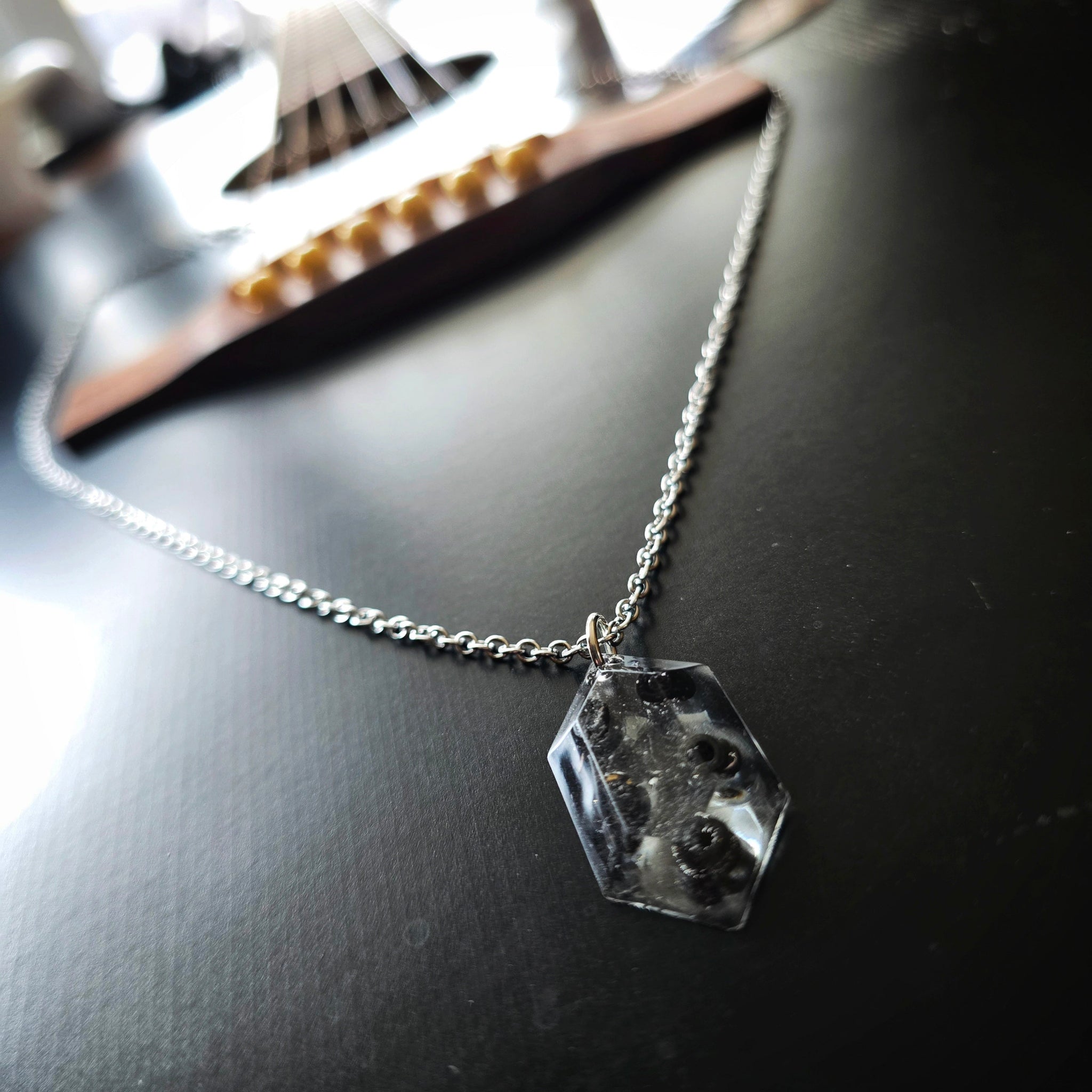 Side Close-up Necklace with a resin hexagonal pendant with black guitar string ballends on a dark guitar