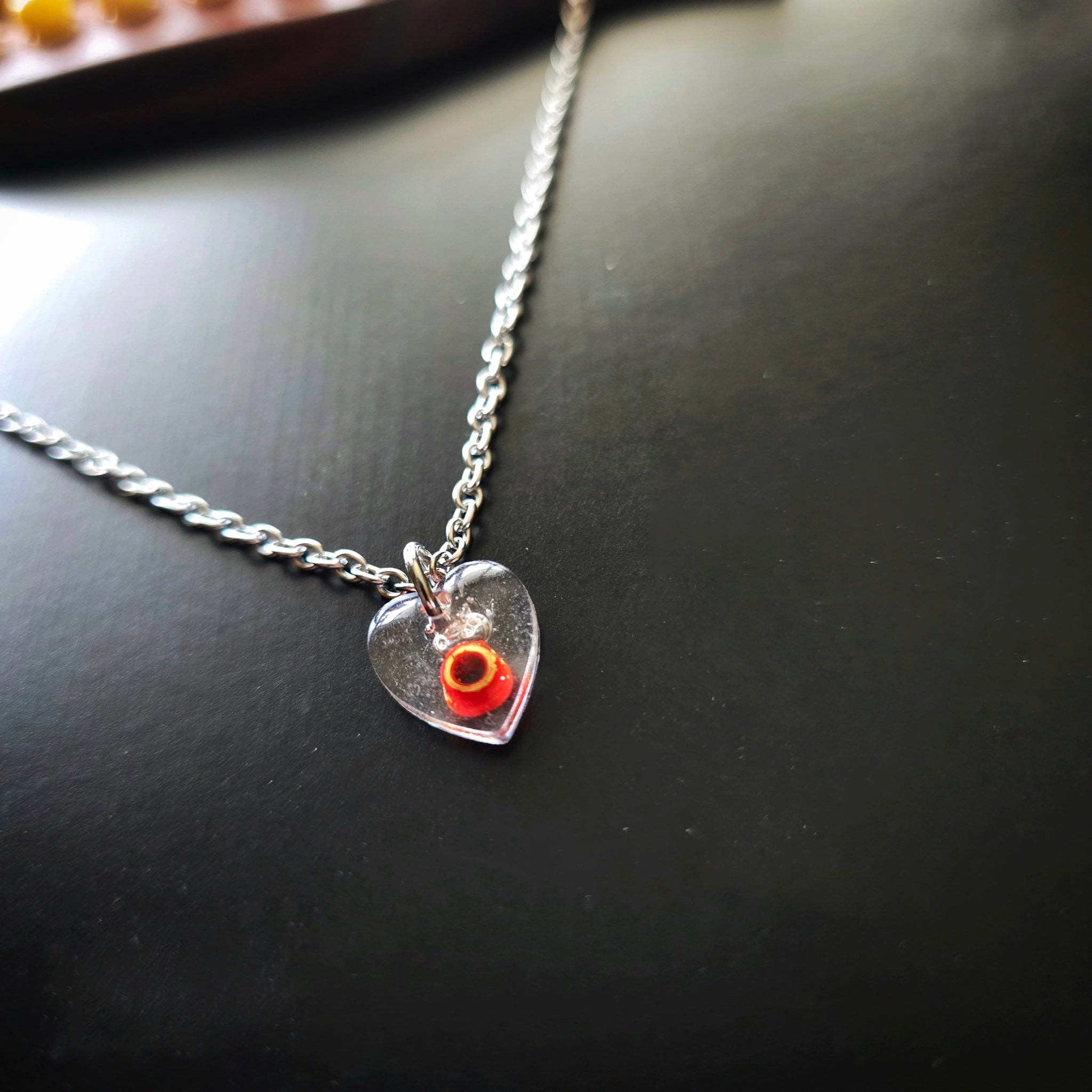 Side Close-up of Silver necklace with a red ballend in a resin heart-shaped pendant on a guitar