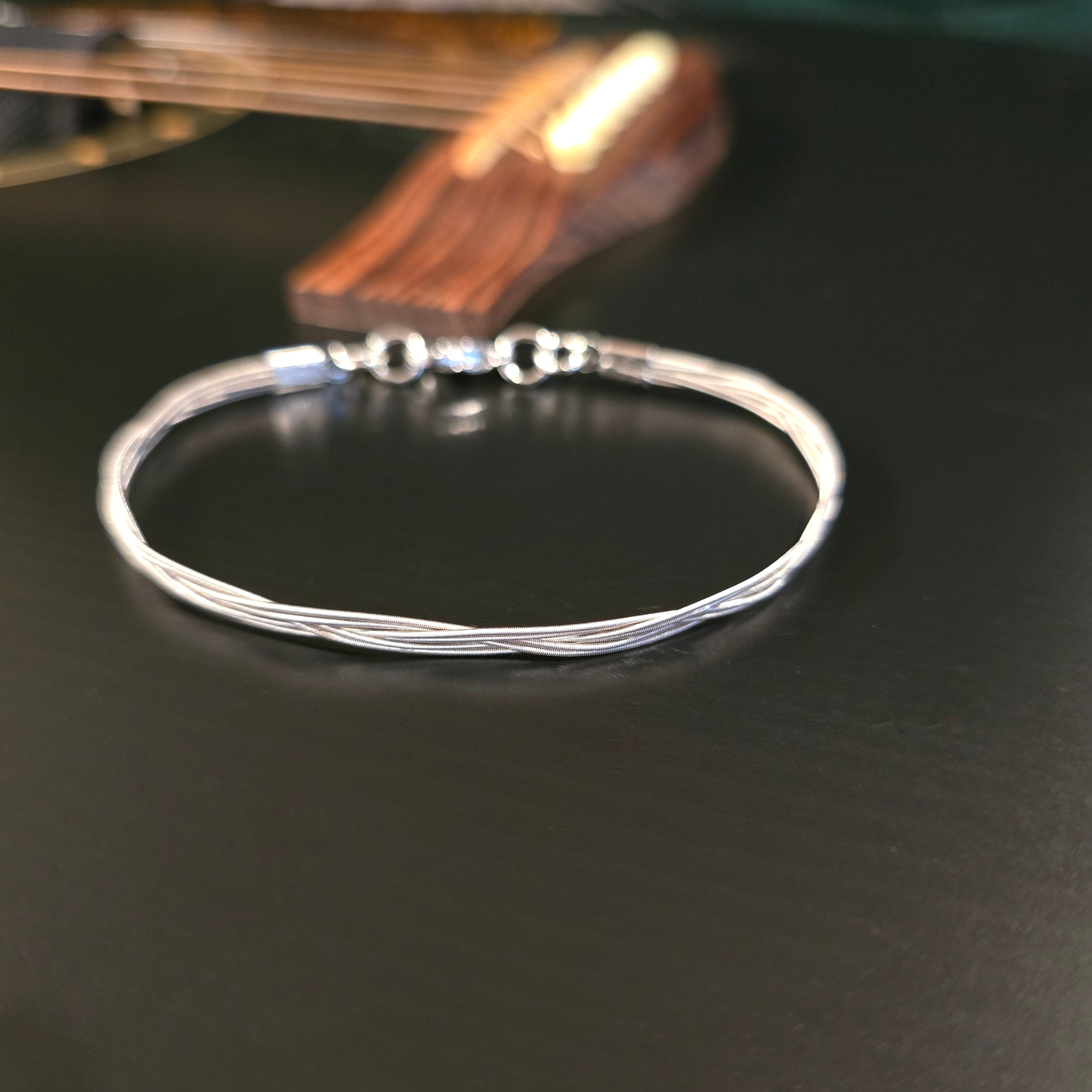 Silver coloured six string guitar string bracelet on black guitar 
