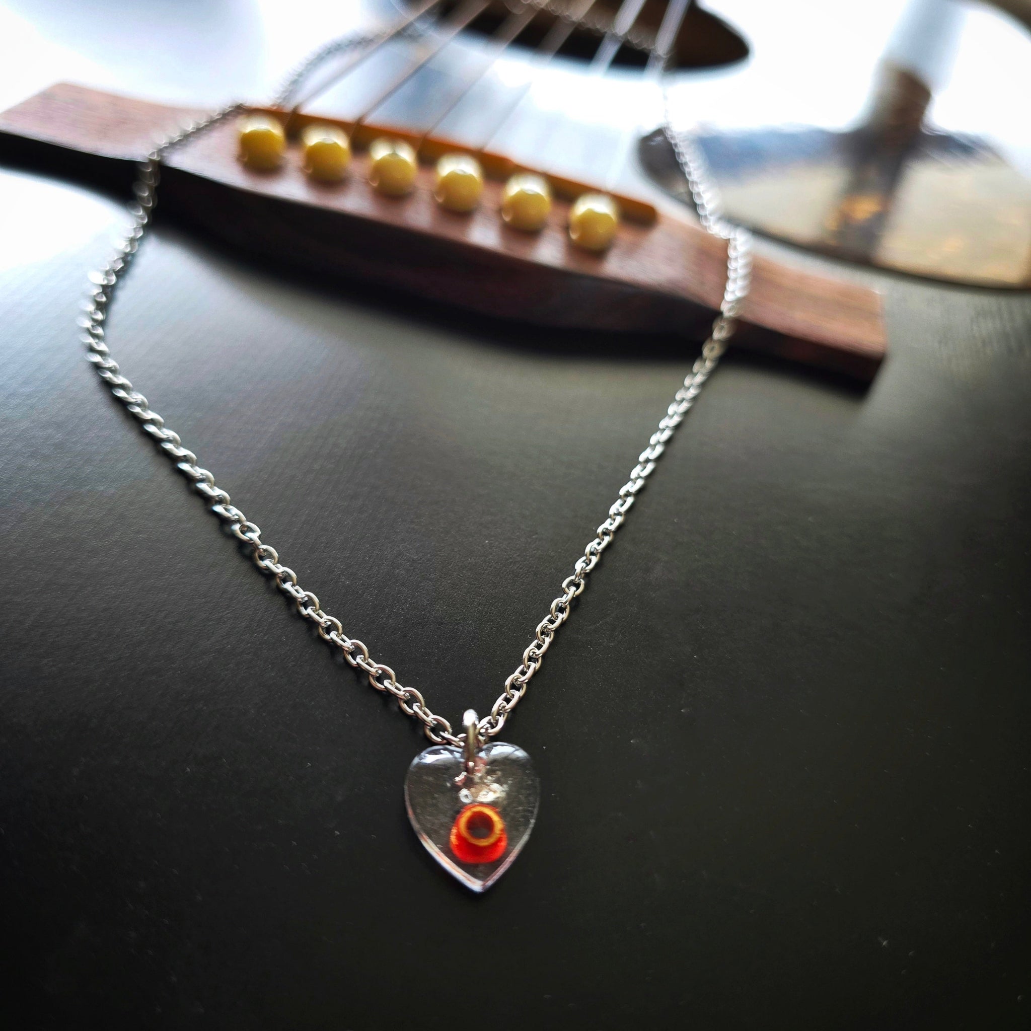 Silver necklace with a red ballend in a resin heart-shaped pendant on a guitar