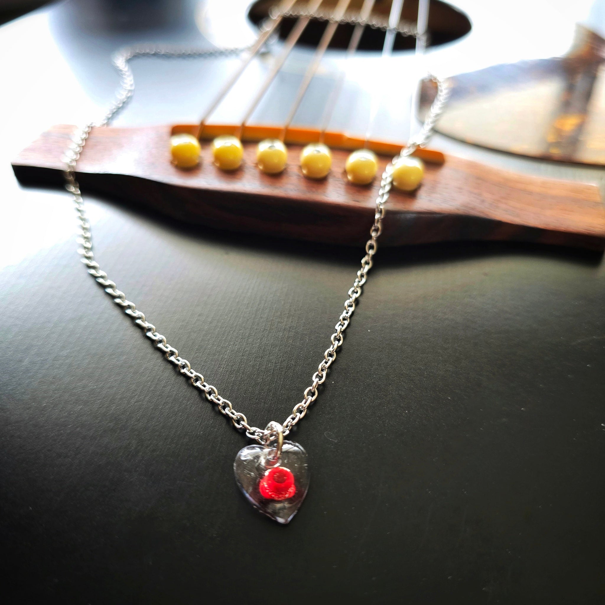 Silver necklace with a red ballend in a resin heart-shaped pendant on a guitar Long View