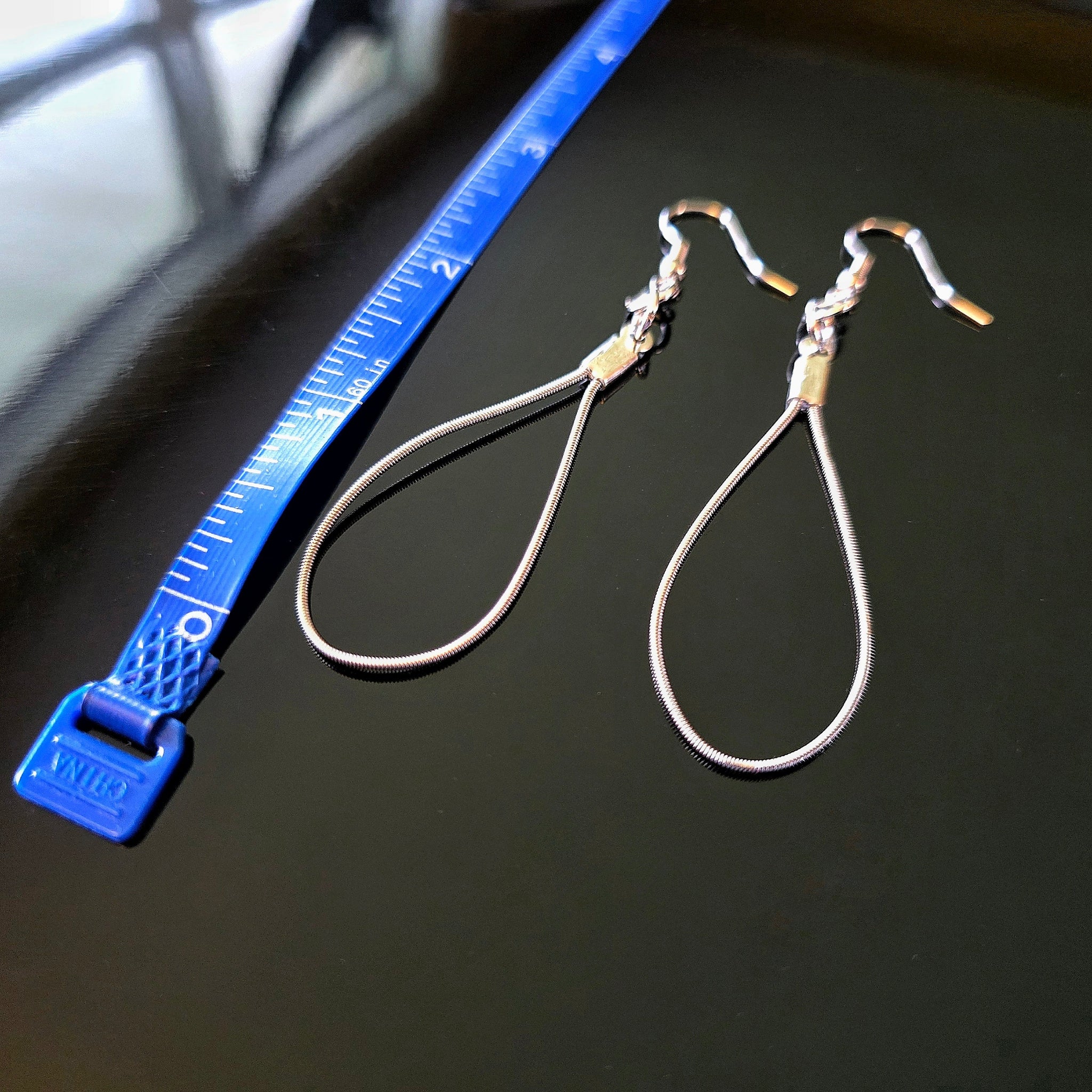 Teardrop Guitar String Earrings on Black Background and Blue Measuring Tape