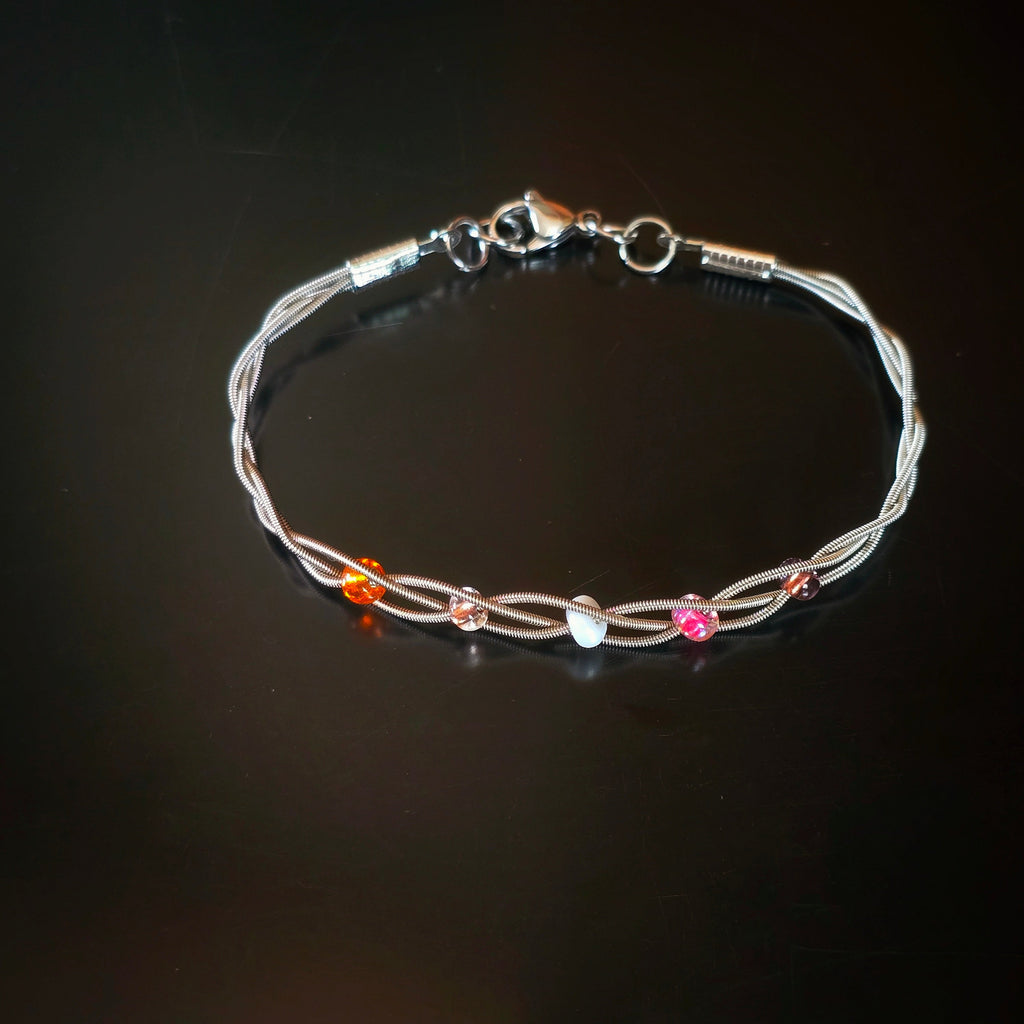 top view of guitar string bracelet with 5 beads representing the colours of the lesbian pride flag dark background