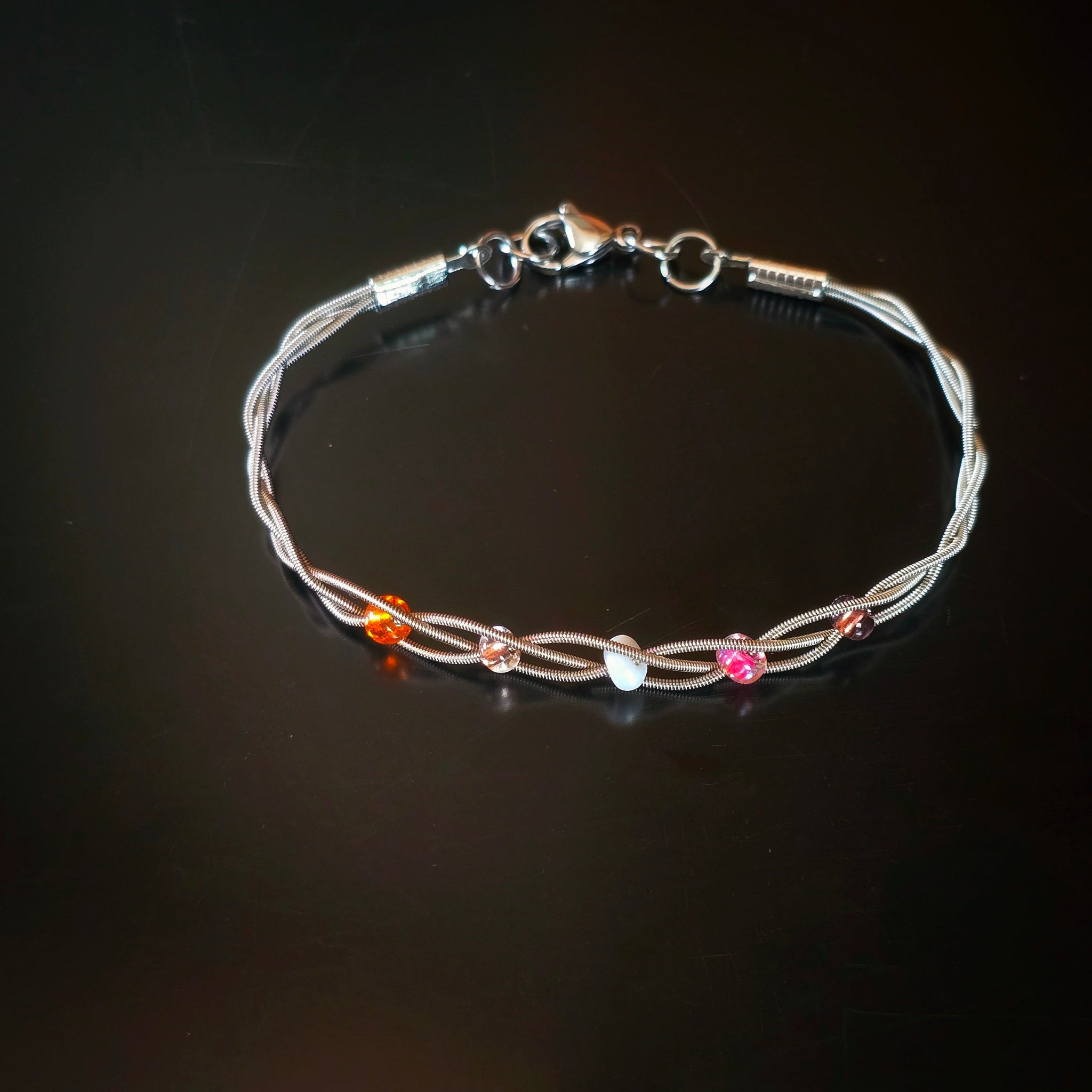 top view of guitar string bracelet with 5 beads representing the colours of the lesbian pride flag dark background