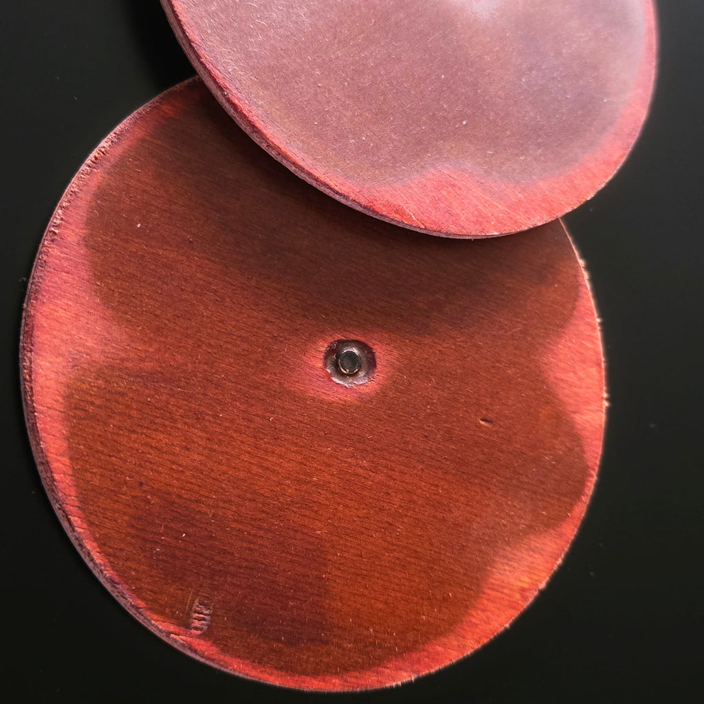 Two round coasters made from guitar woodon a black background