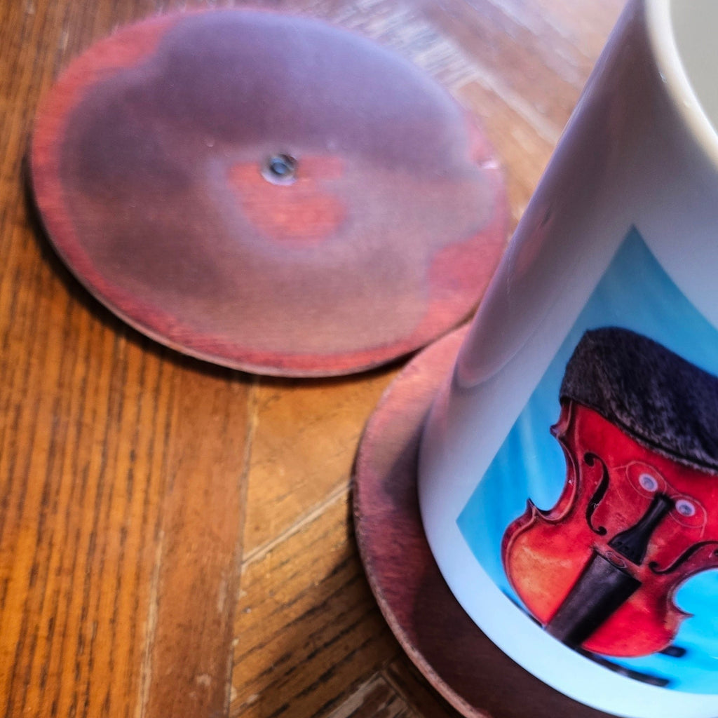 Two round coasters made from guitar wood one with a cup on it. 