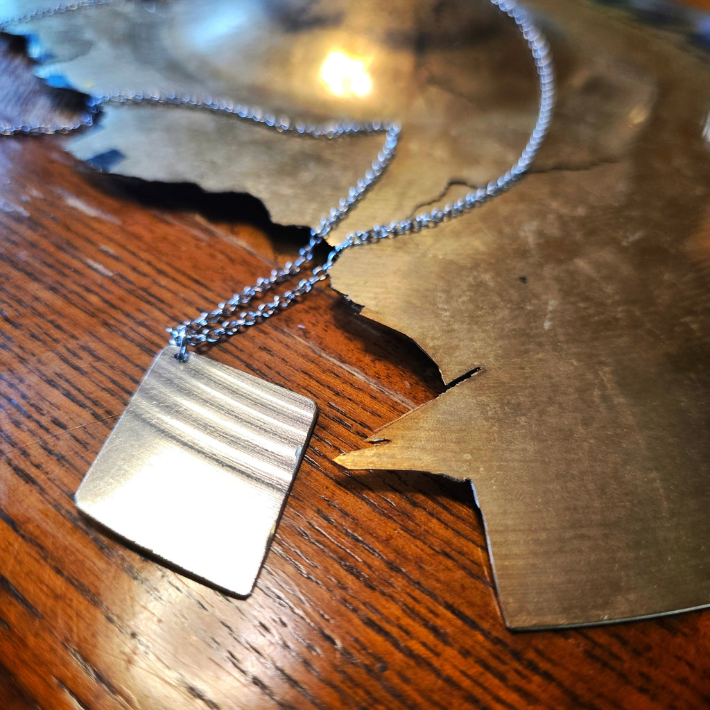 Upcycled Diamond Shaped Cymbal Piece Necklace beside Broken Cymbal