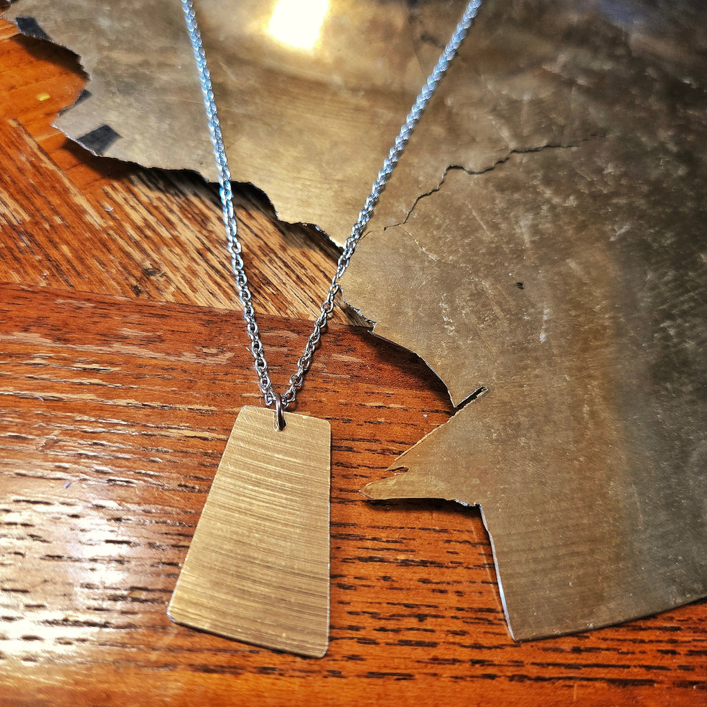 Upcycled Rectangle Shaped Cymbal Piece Necklace beside Broken Cymbal
