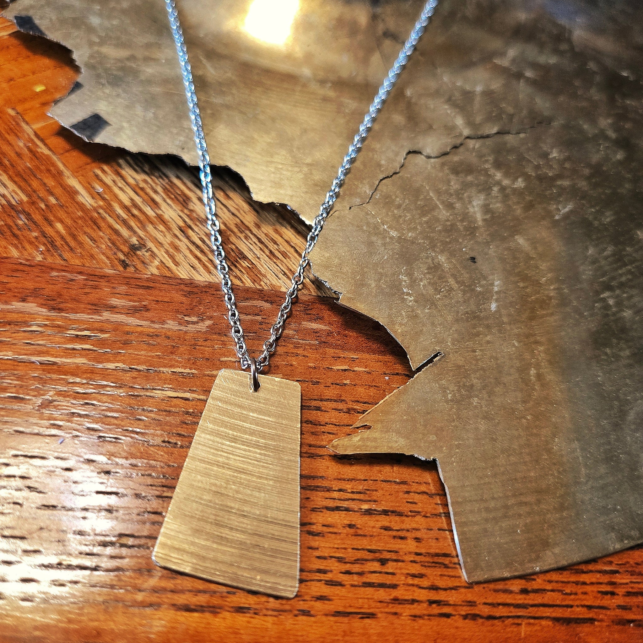 Upcycled Rectangle Shaped Cymbal Piece Necklace beside Broken Cymbal