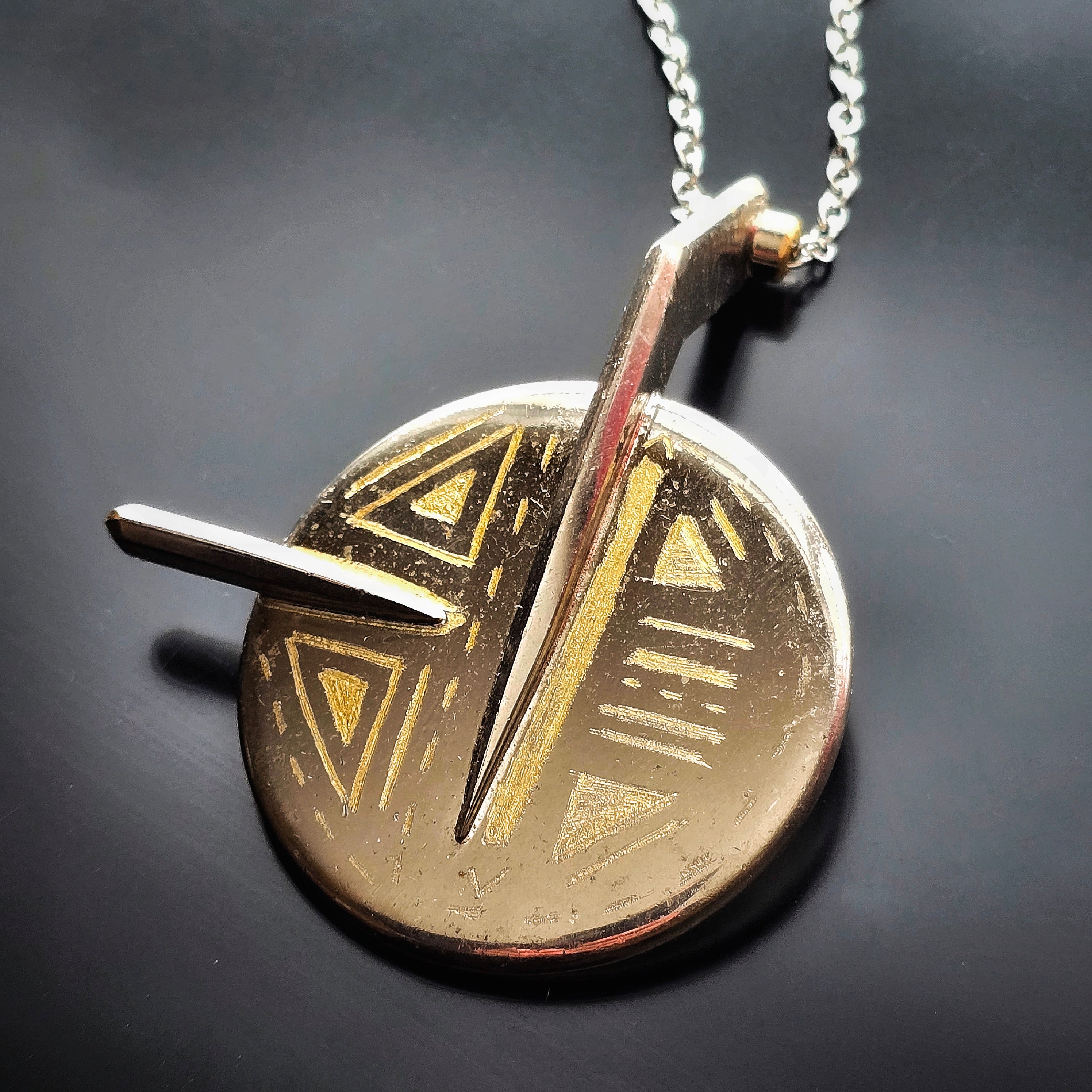 Upcycled saxophone key pendant necklace on a dark background