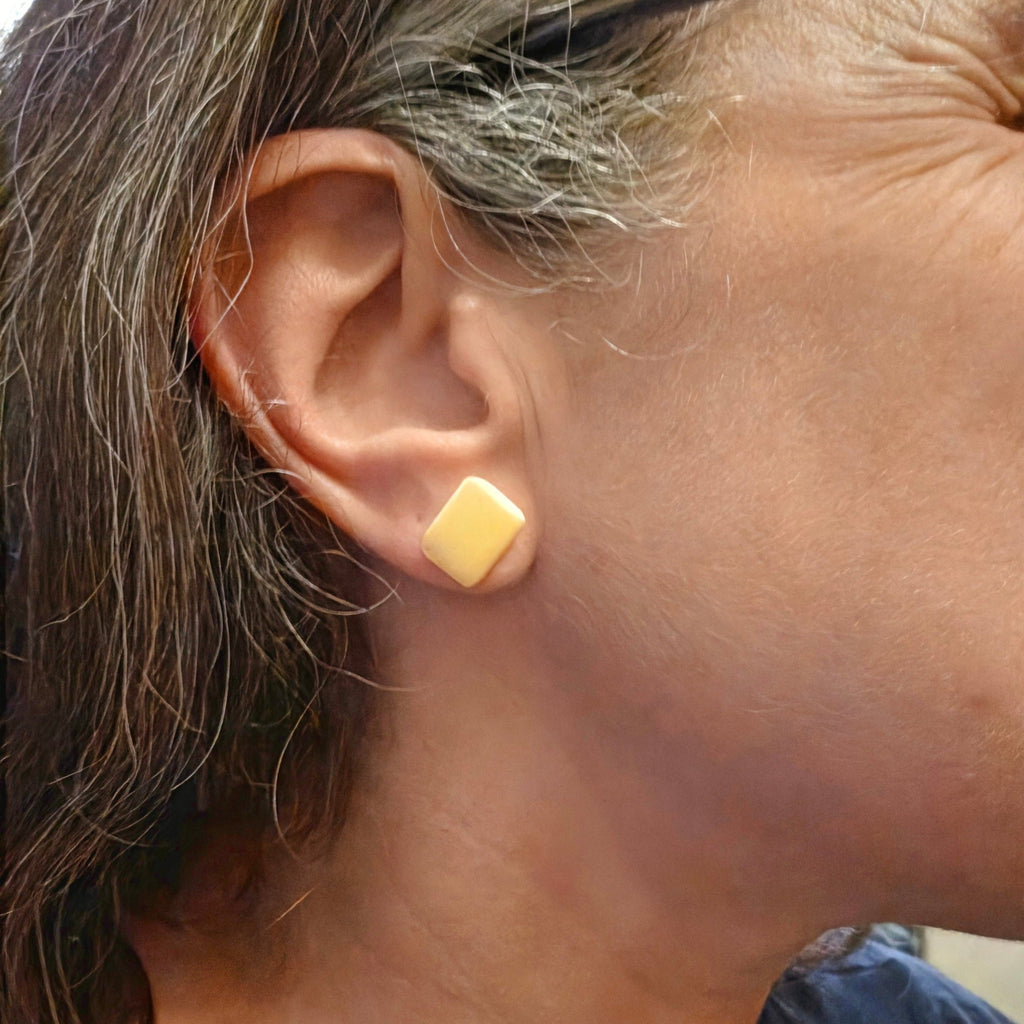 A close-up side view of a woman's ear wearing a small pair of piano ivory stud earring.