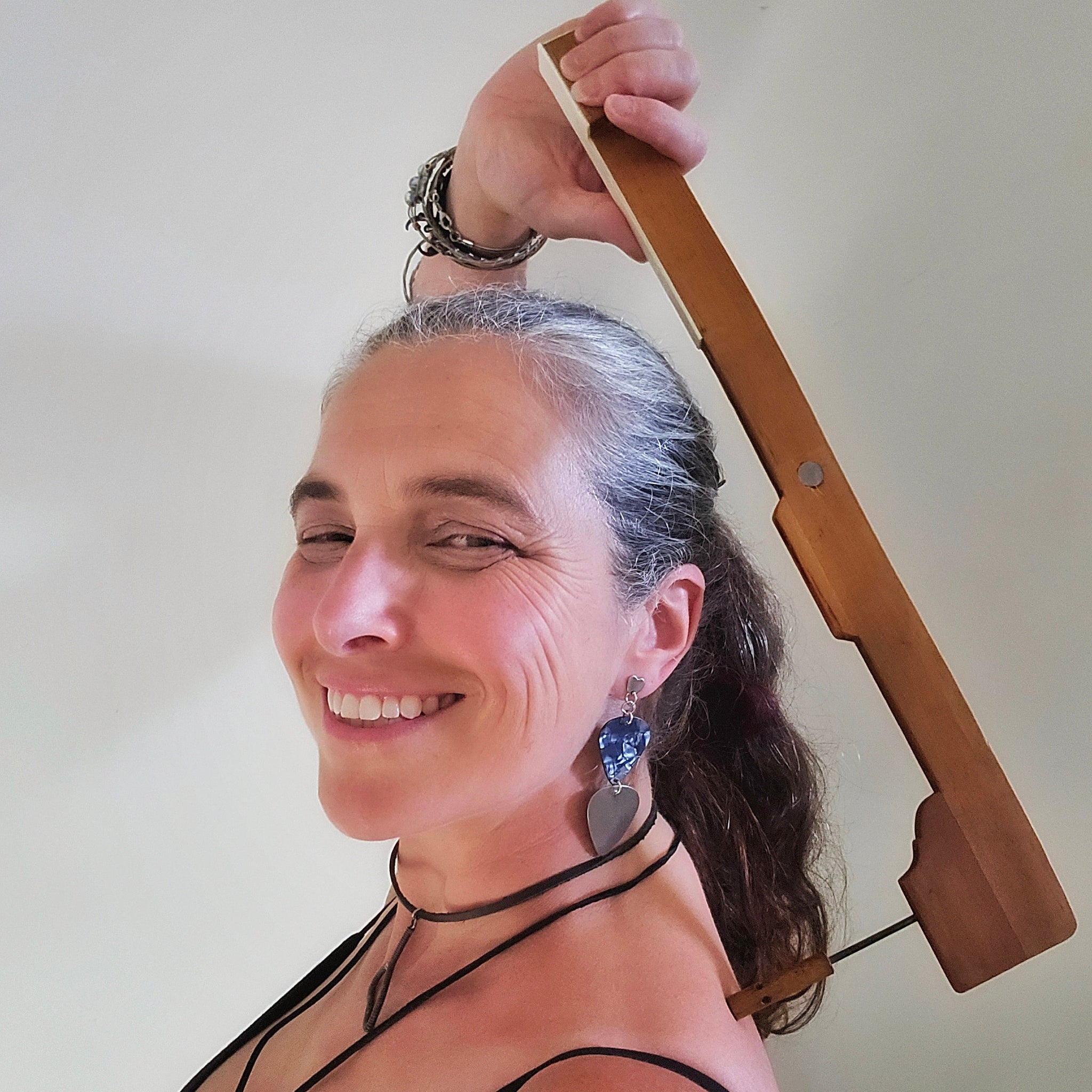 Woman holding a backscratcher made from a piano key against a plain background