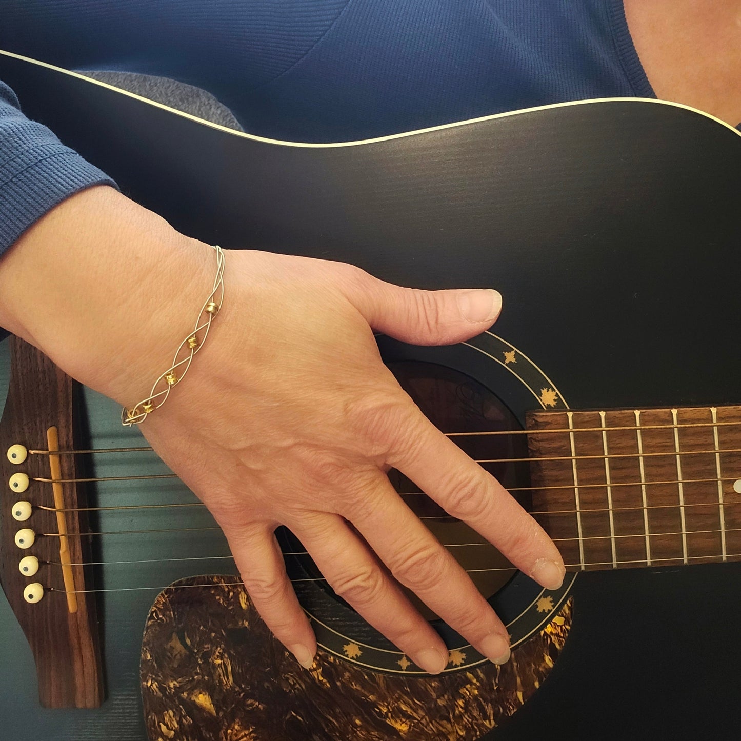 Woman playing guitar wearing upcycled guitar string bracelet