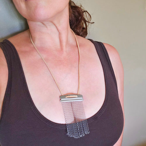A close-up of a woman wearing a snare drum string fringe style suede cord necklace paired with a dark brown tank top.