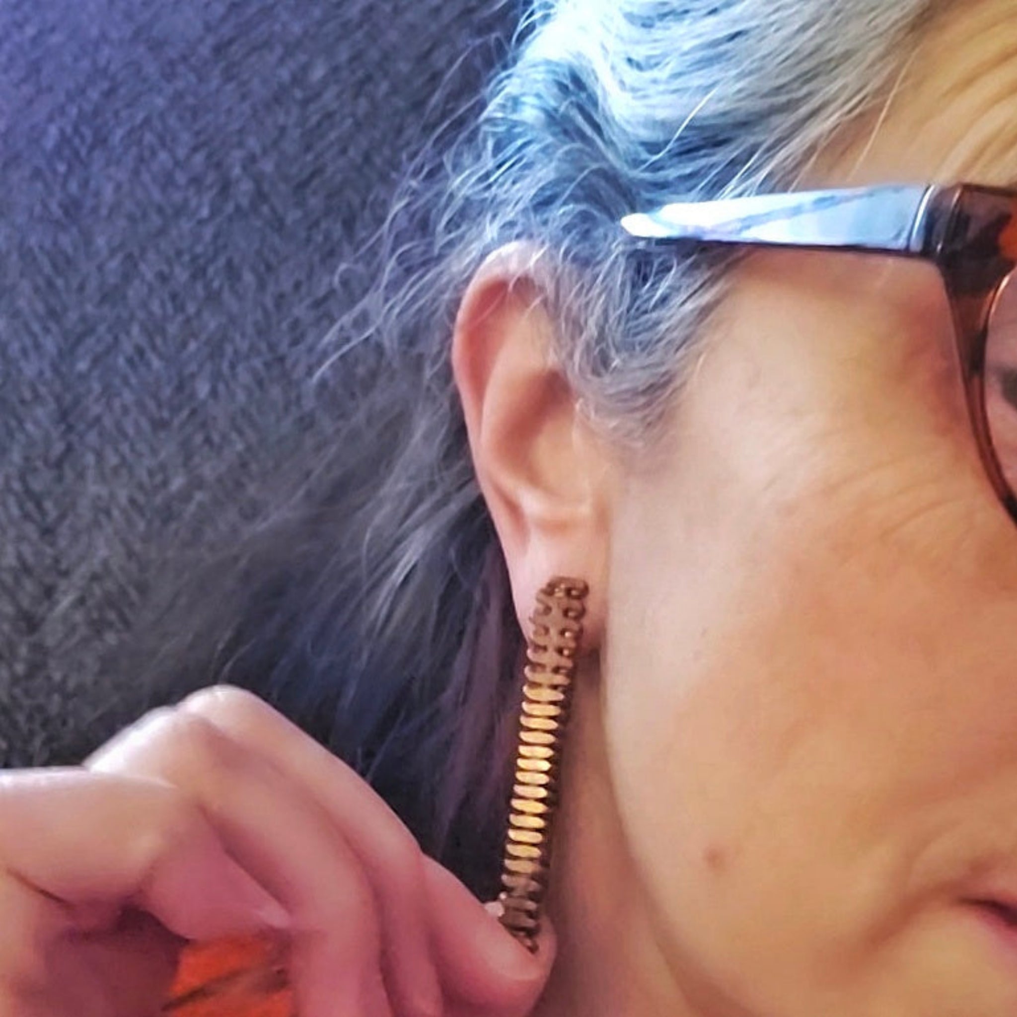 Woman with glasses wearing upcycled copper piano string earrings 