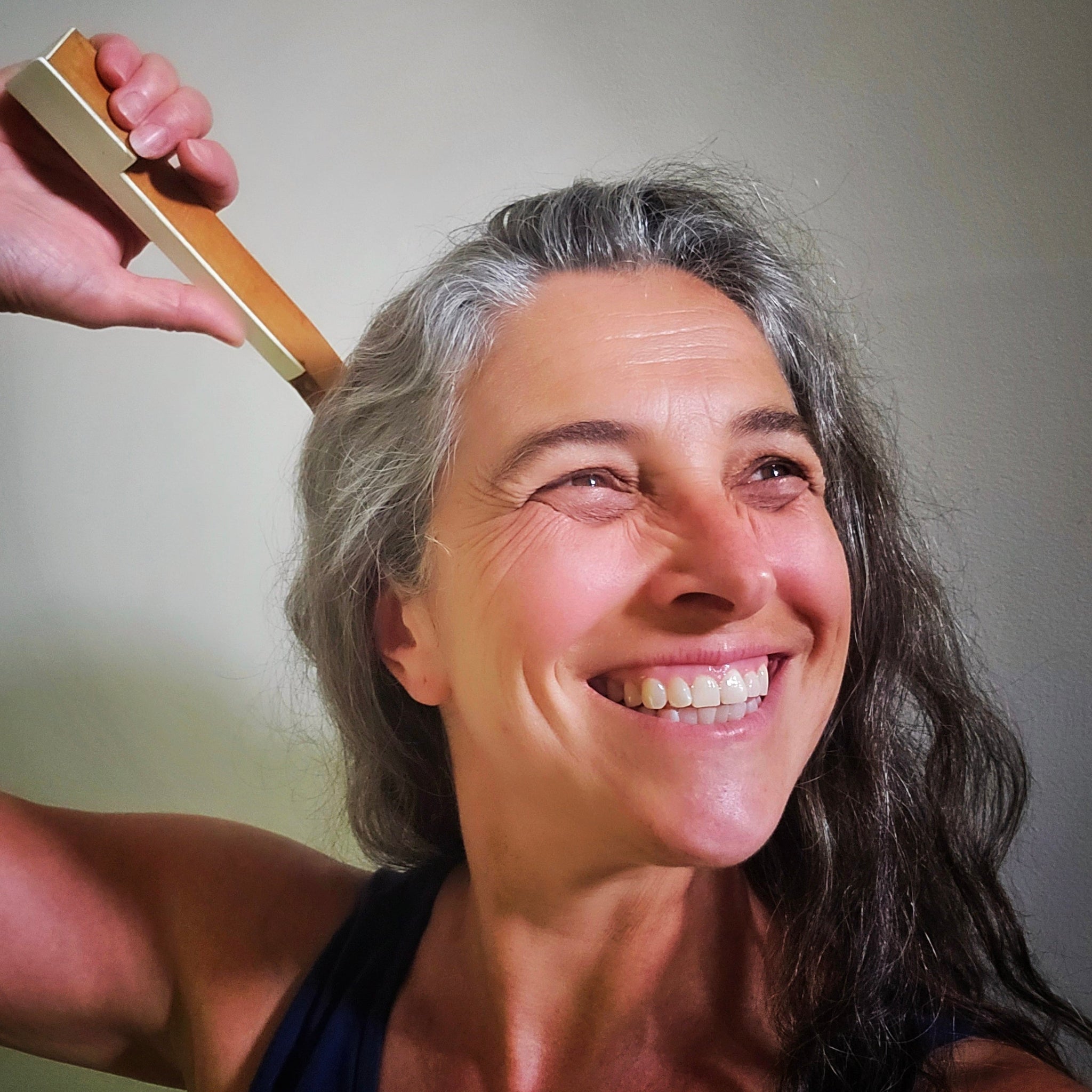Woman with gray hair smiling as a she scratches her back with an upcycled piano key backscratcher