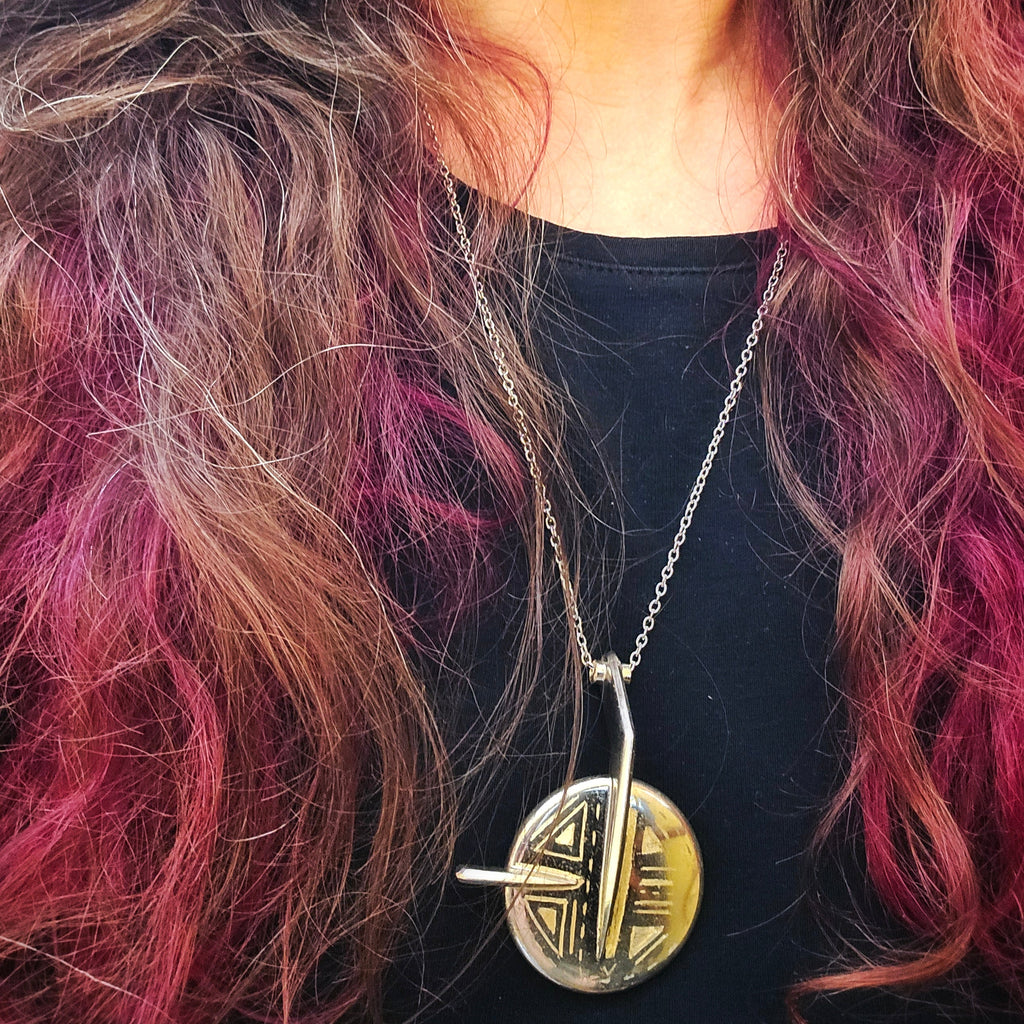 Woman with long, wavy hair wearing a necklace with an upcycled saxophone key pendant.