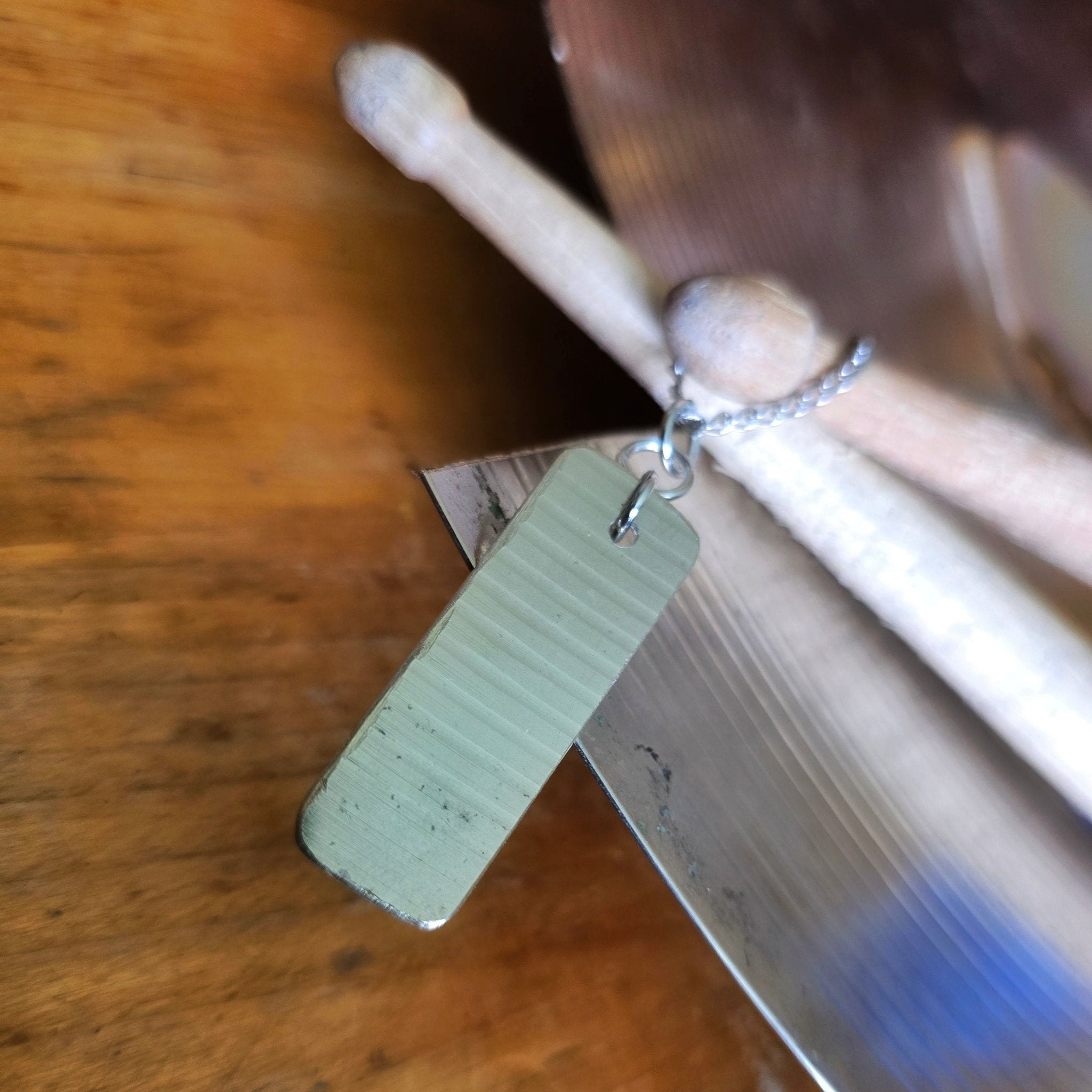 dog tag style upcycled cymbal piece necklace on drumsticks and a broken cymbal 