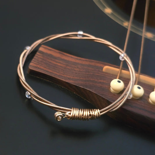 bronze coloured guitar string bangle bracelet with clear glass beads on a guitar