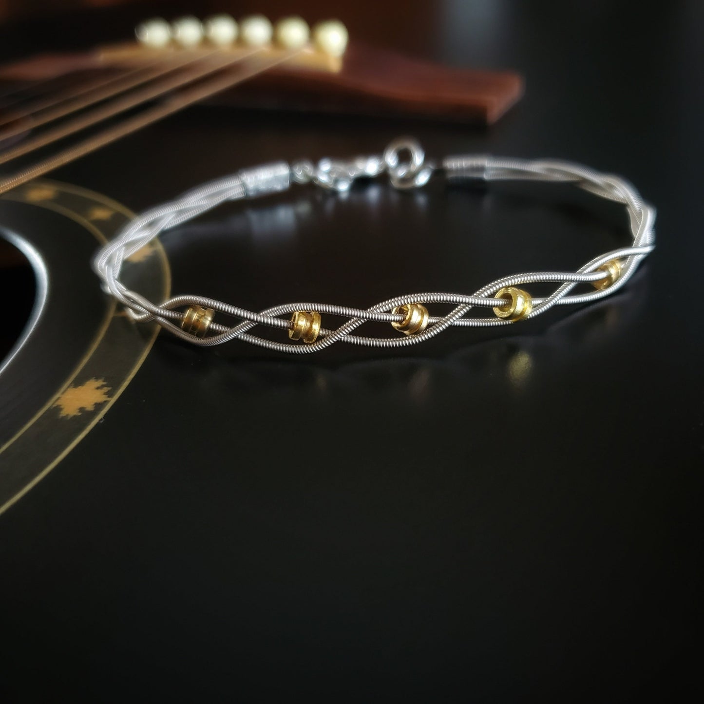 bracelet made with 3 strands of silver coloured guitar strings and 5 gold coloured guitar string ballends on a black background