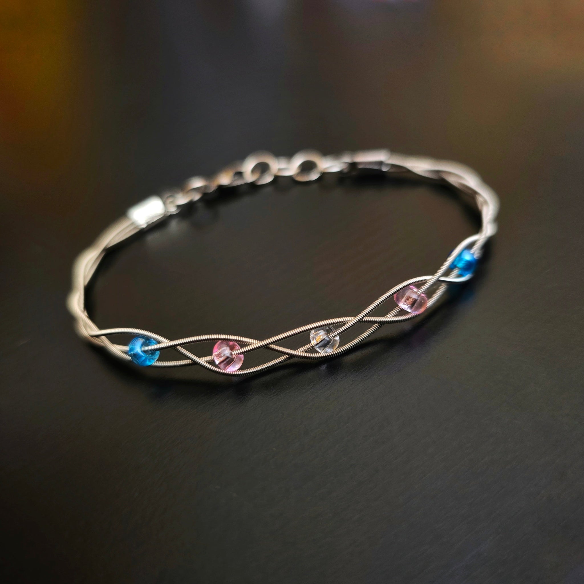 braided trans pride guitar string bracelet on black background