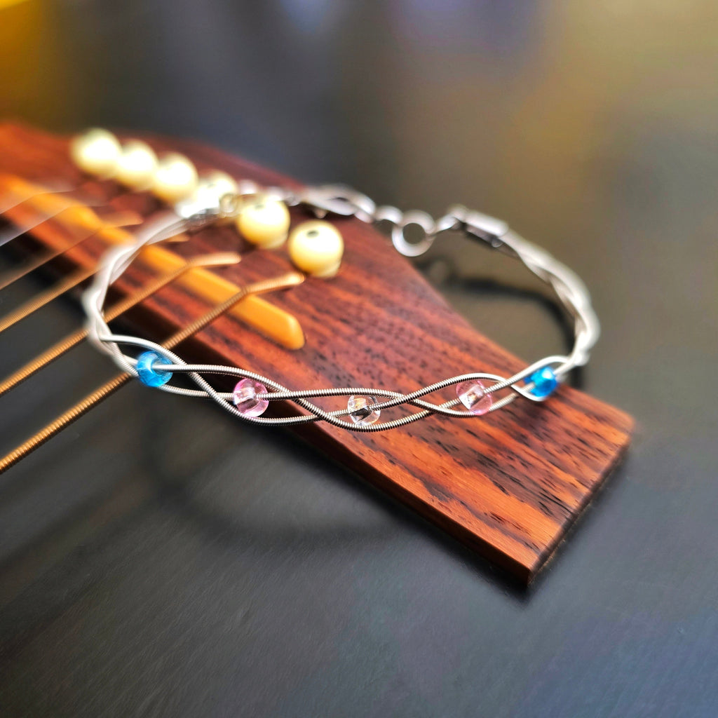 braided trans pride guitar string bracelet on black guitar bridge