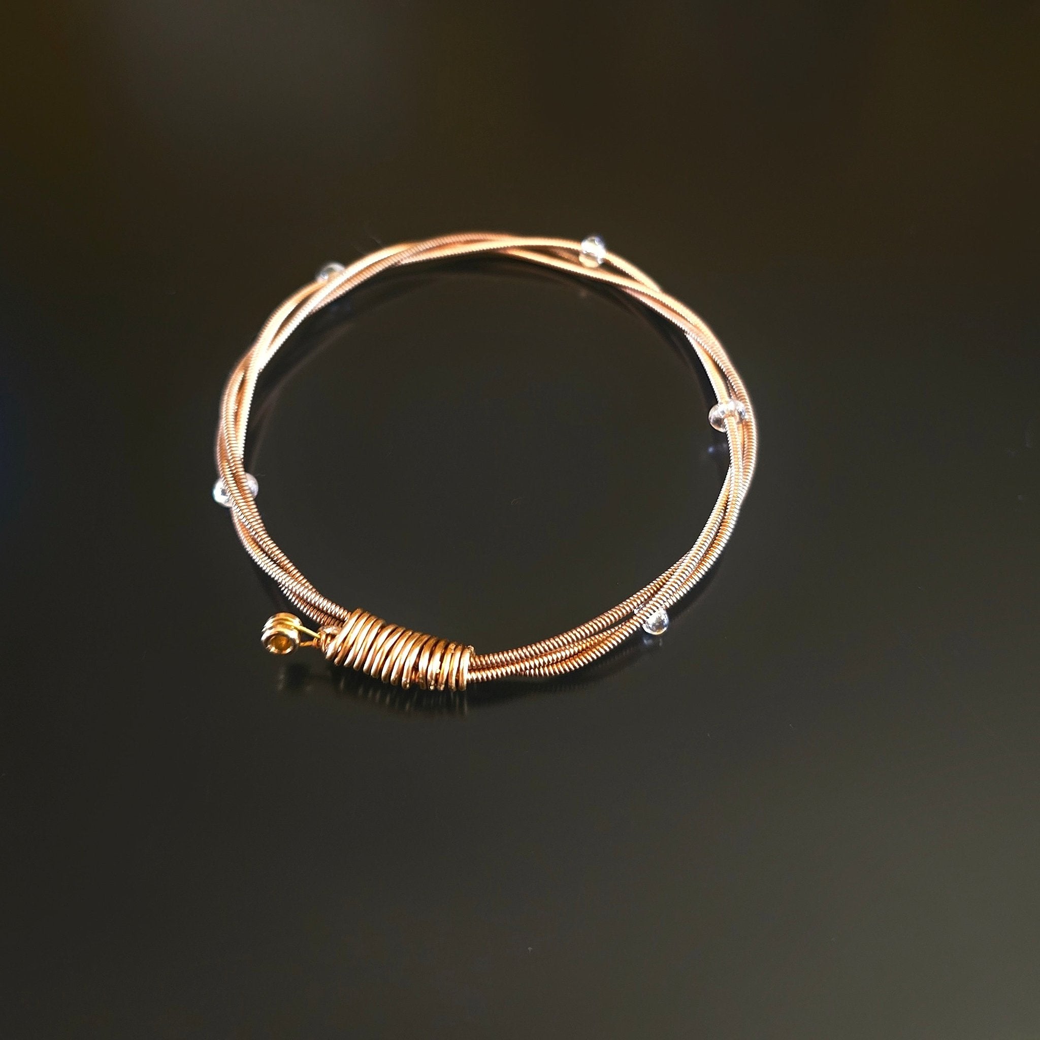 bronze coloured guitar string bangle bracelet with clear glass beads on a black background