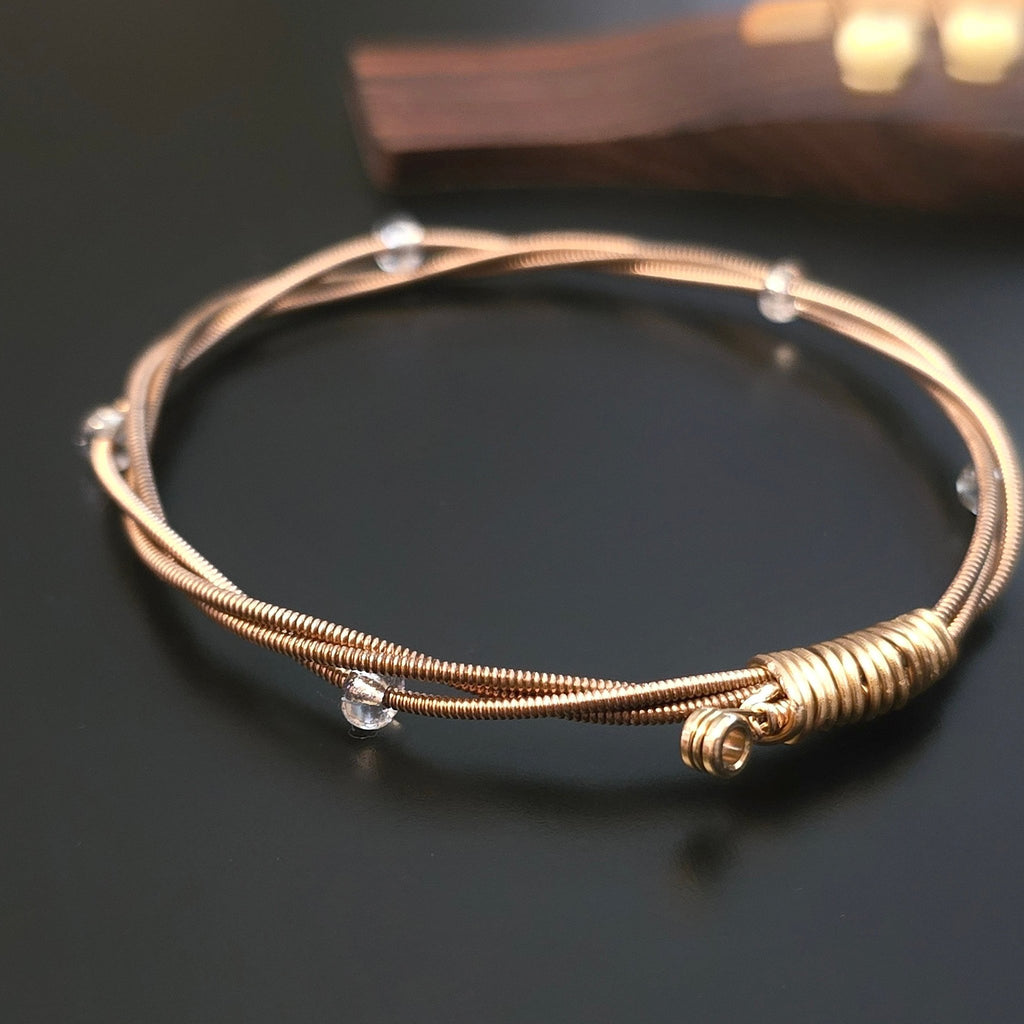 bronze coloured guitar string bangle bracelet with clear glass beads on a black guitar